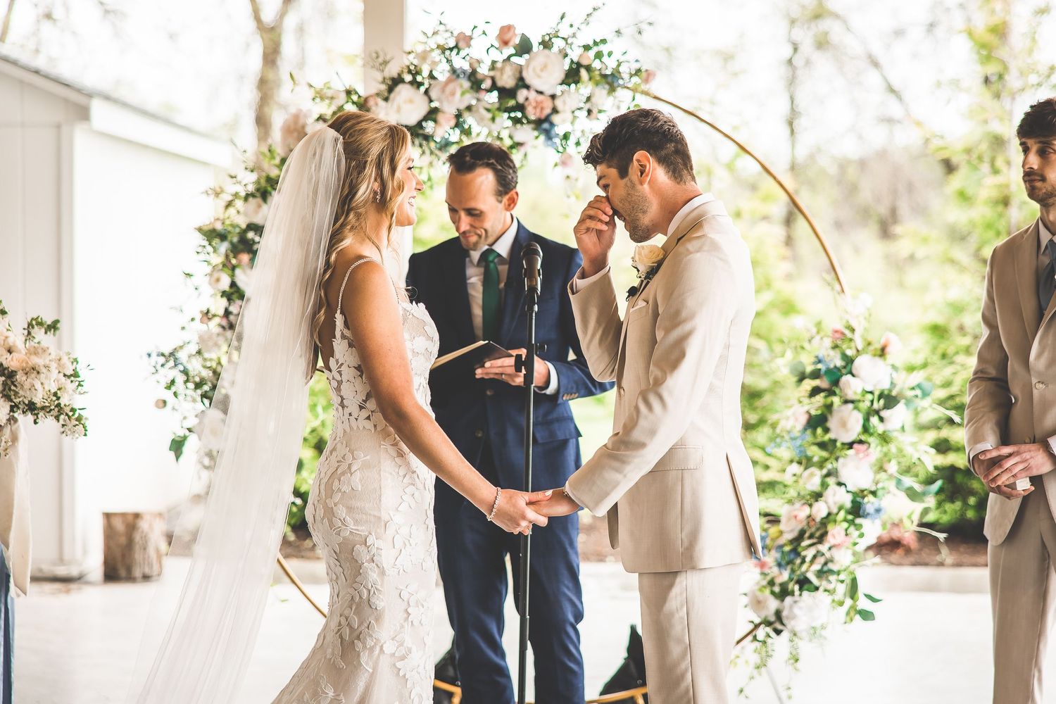 Couple shares emotional moment under floral arch during wedding ceremony.