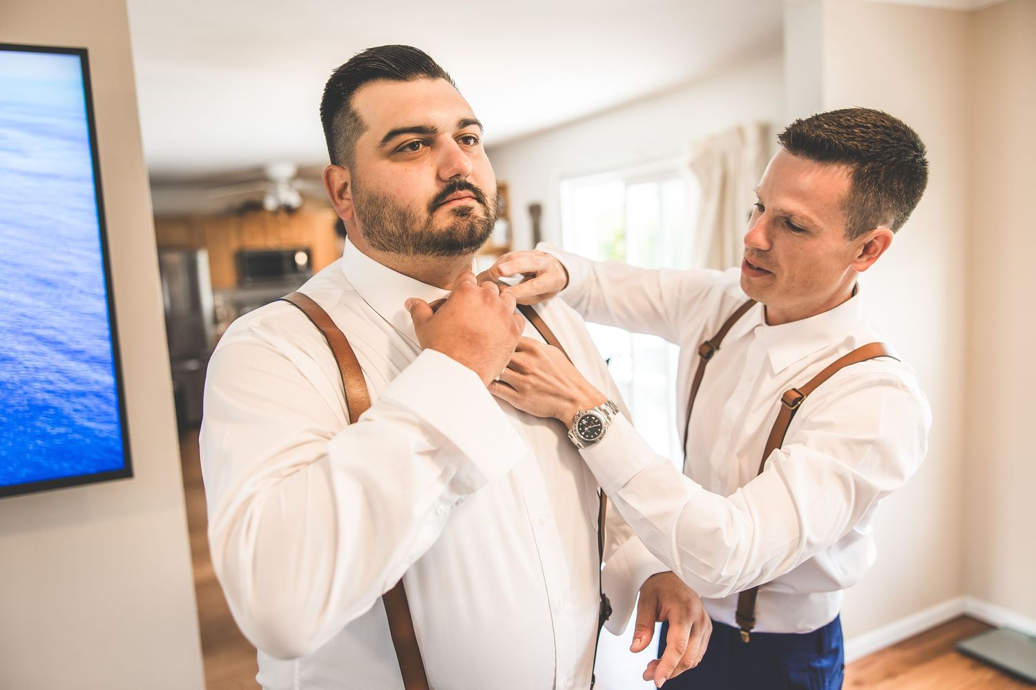 Men in white shirts and suspenders preparing for formal event.
