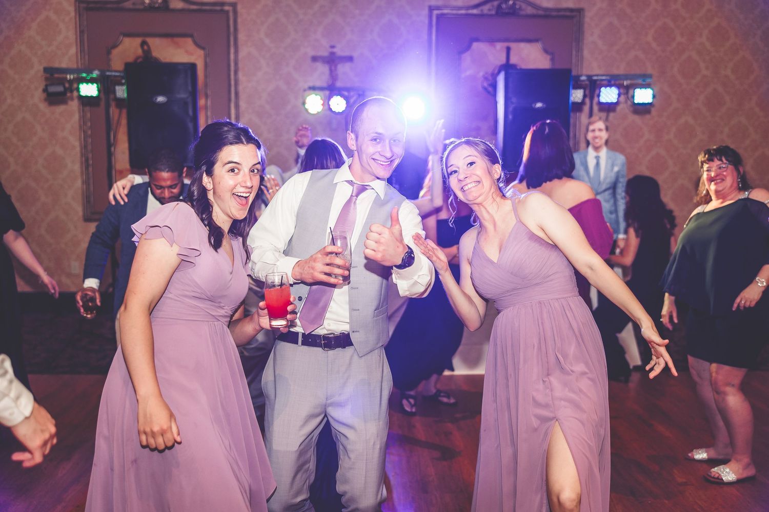 Wedding guests dancing under purple spotlights in an elegant reception hall.