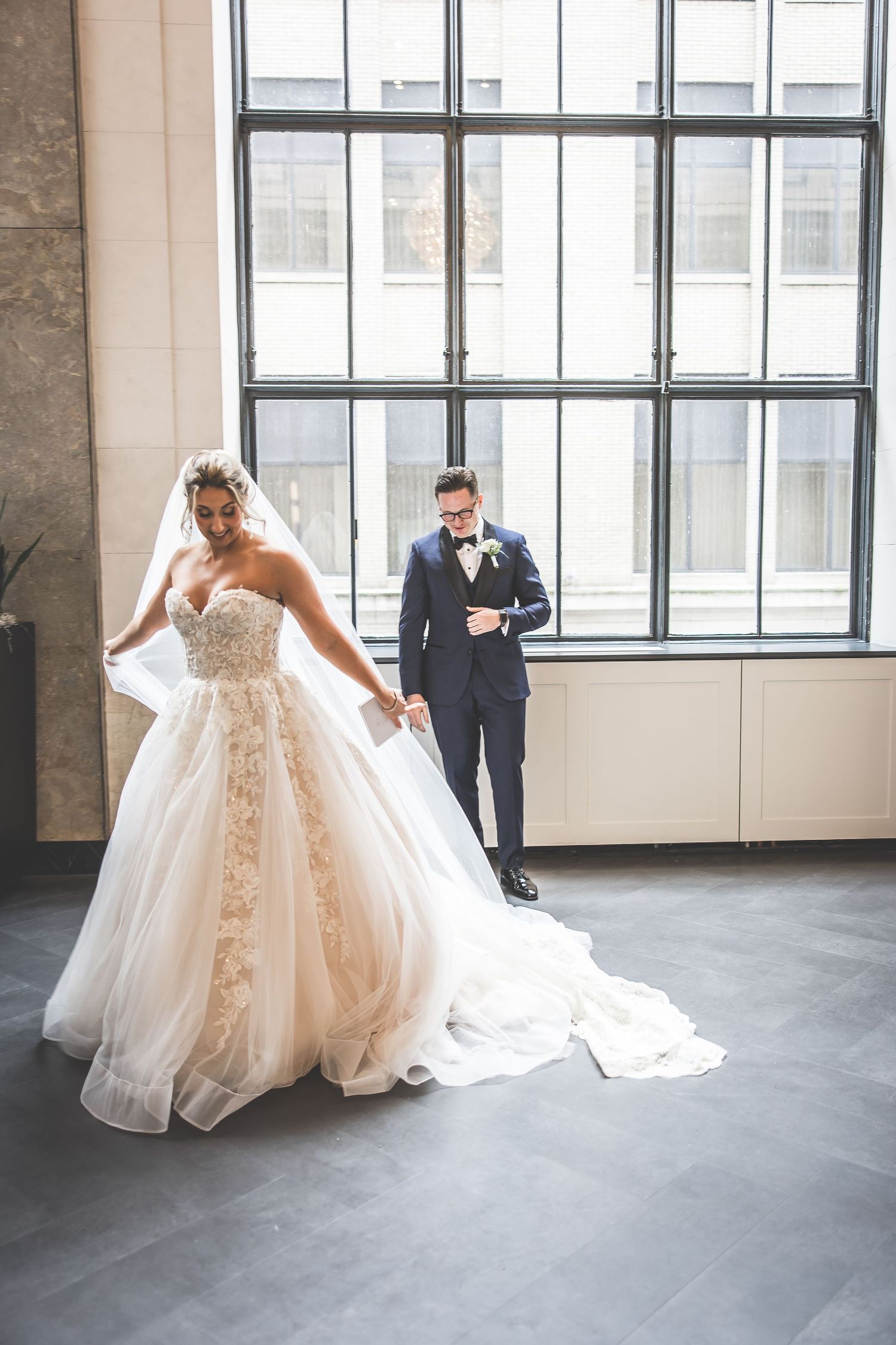 Bride in flowing ballgown twirls in front of industrial windows.