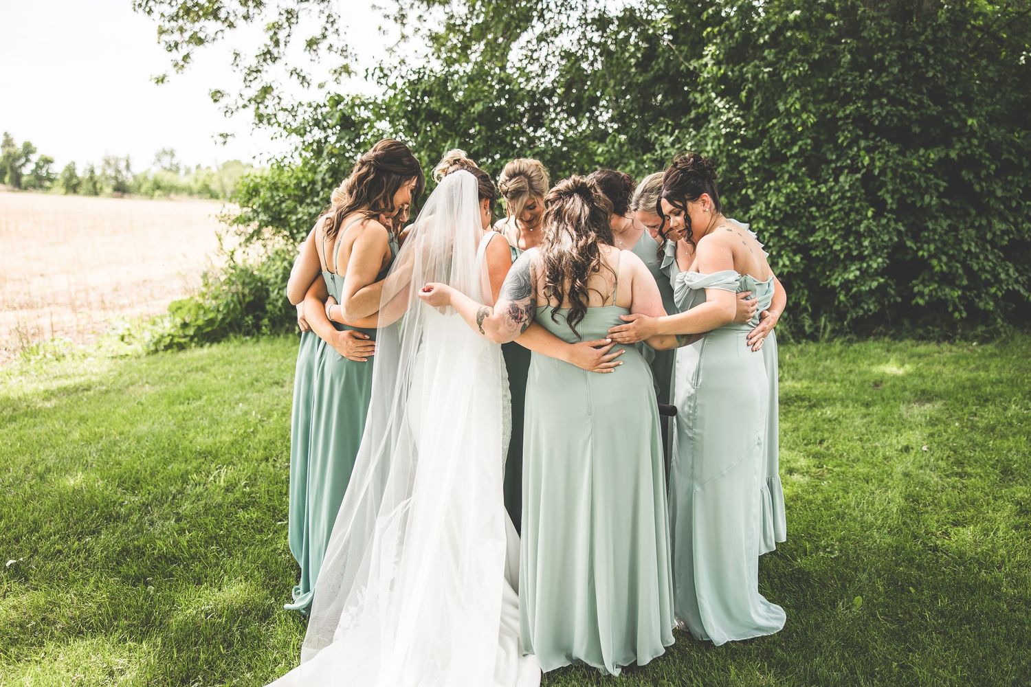 Wedding party in mint green dresses gathered on a grassy hillside.