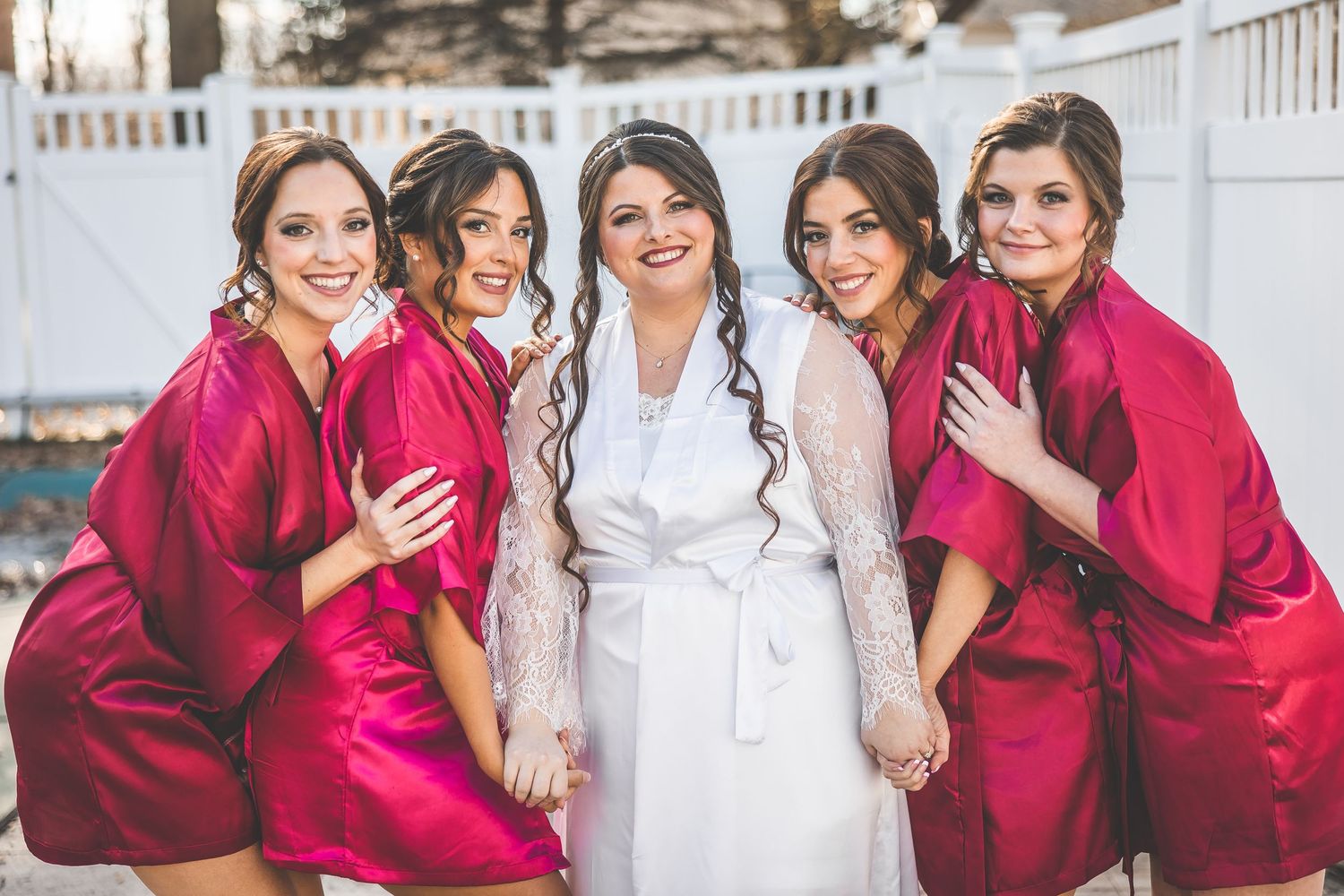 Bridesmaids in bright red dresses posing with the bride in white against a light background.