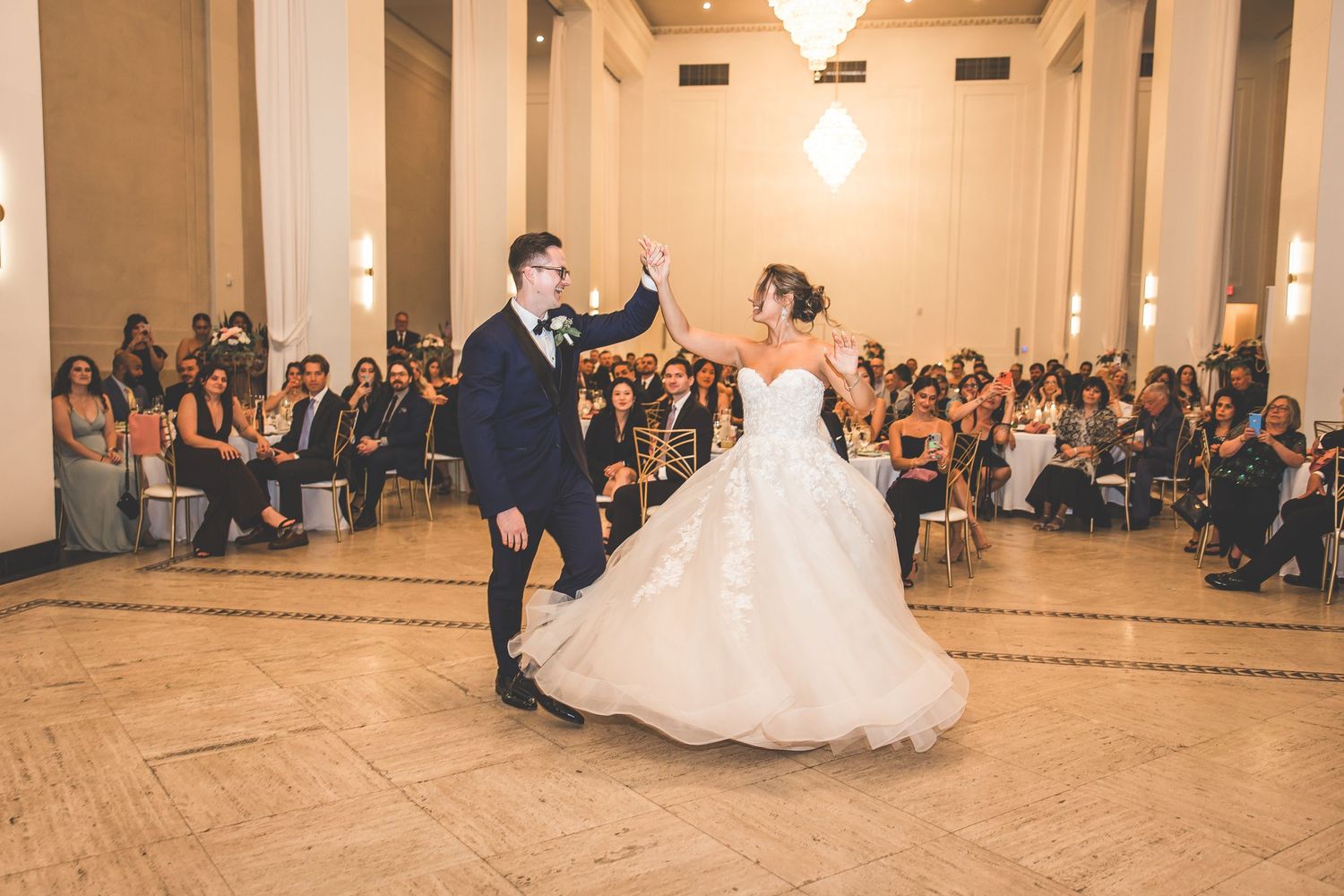 Couple executes dramatic dance moves on elegant ballroom floor surrounded by guests.