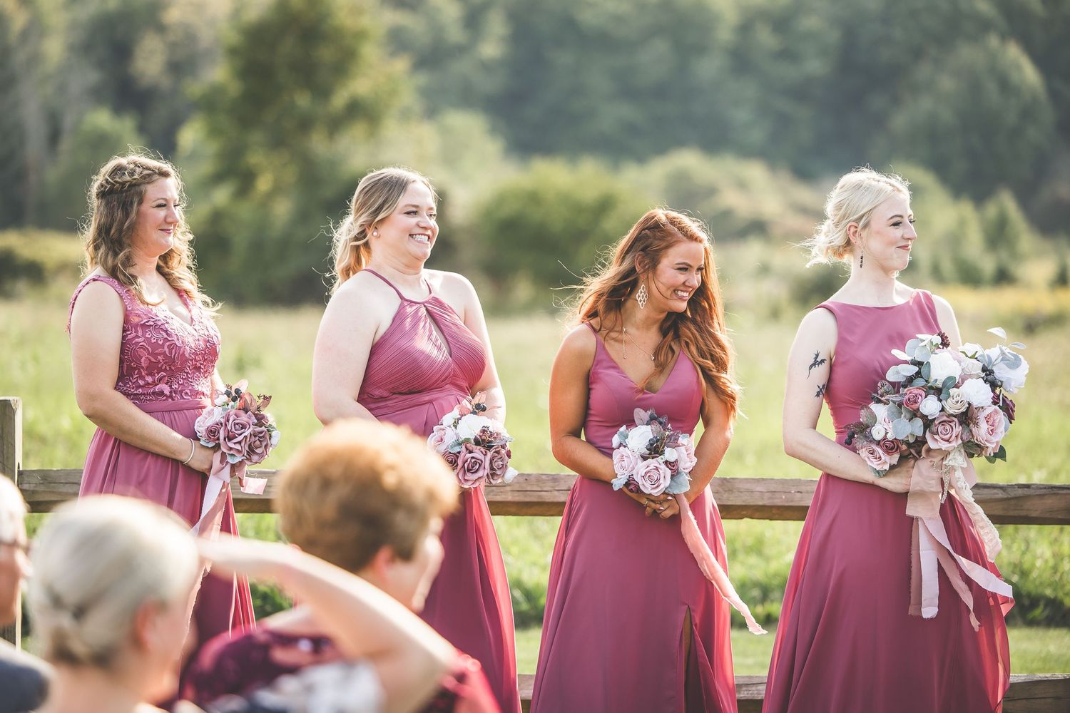 Bridesmaids in dusty rose dresses holding bouquets at outdoor wedding ceremony.
