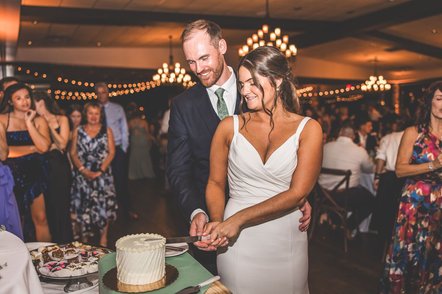 Wedding reception venue with warm lighting and guests gathered around dessert table.