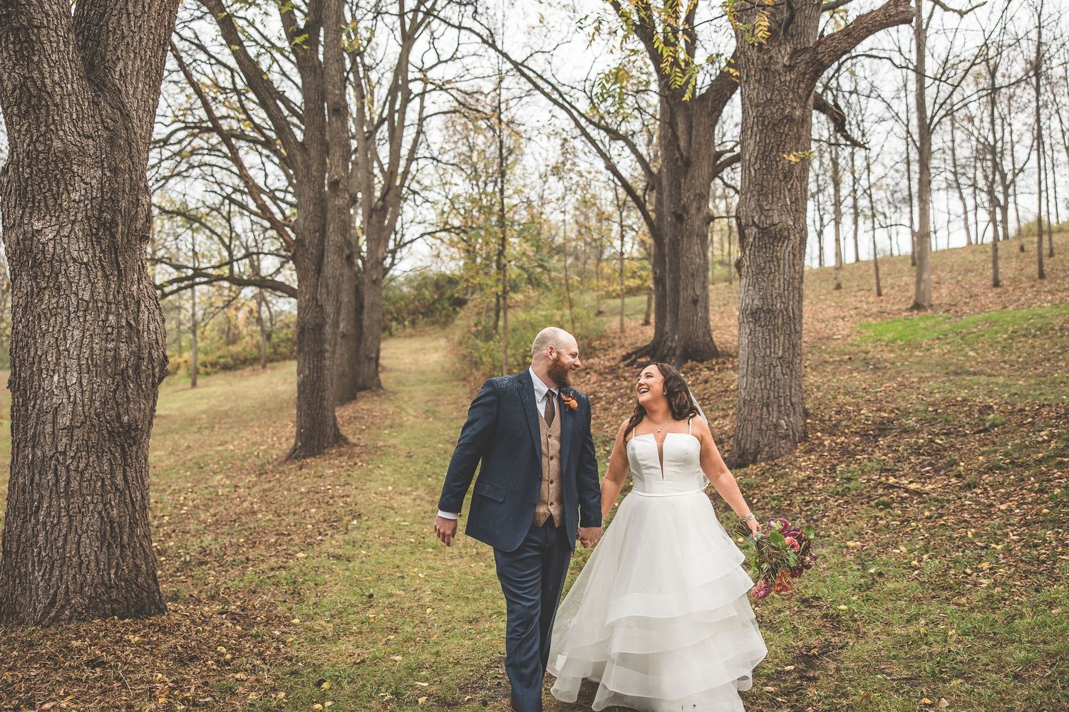 Wedding party poses among tall trees in a natural wooded setting during fall.