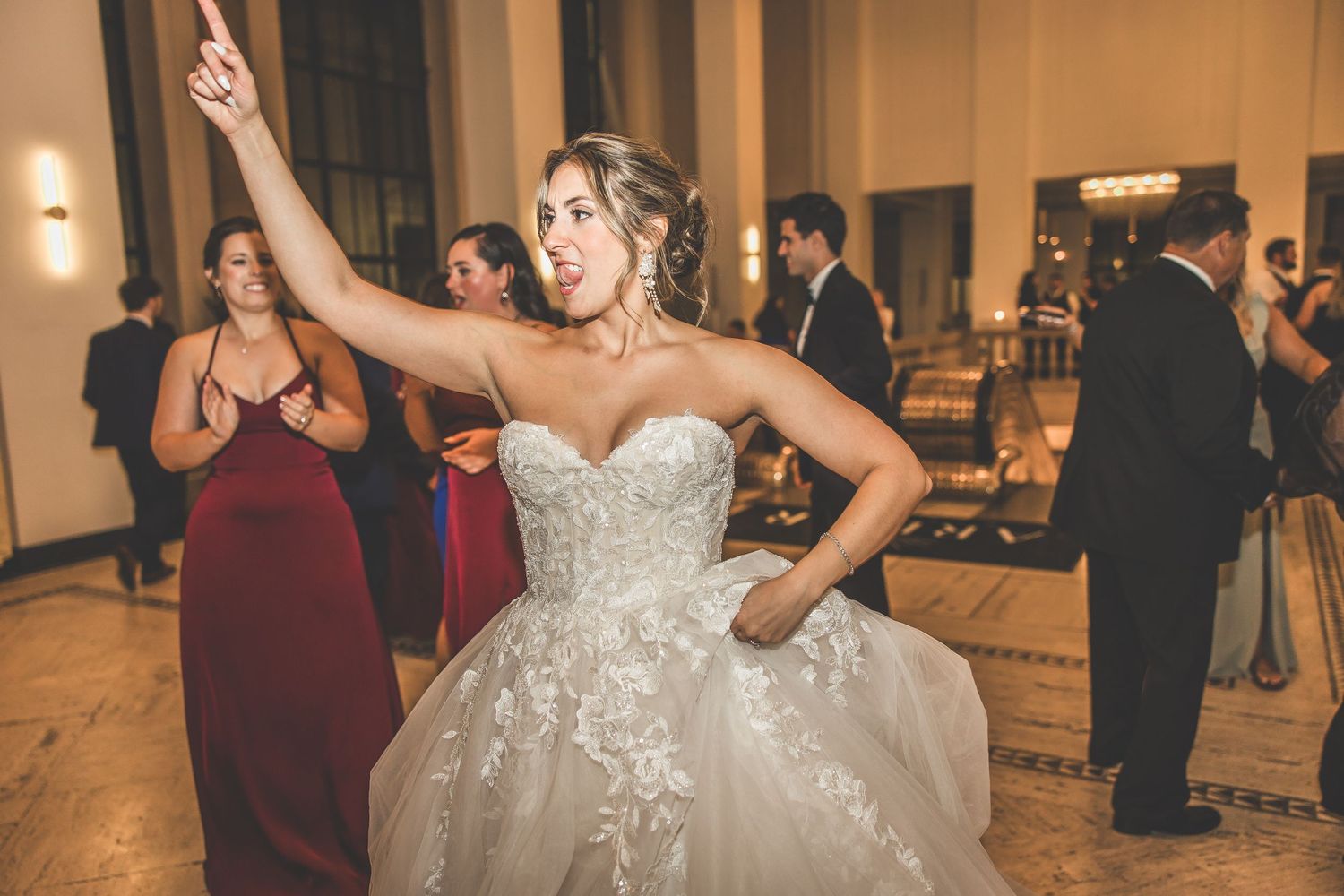 Bride in strapless lace gown dances enthusiastically at wedding reception.