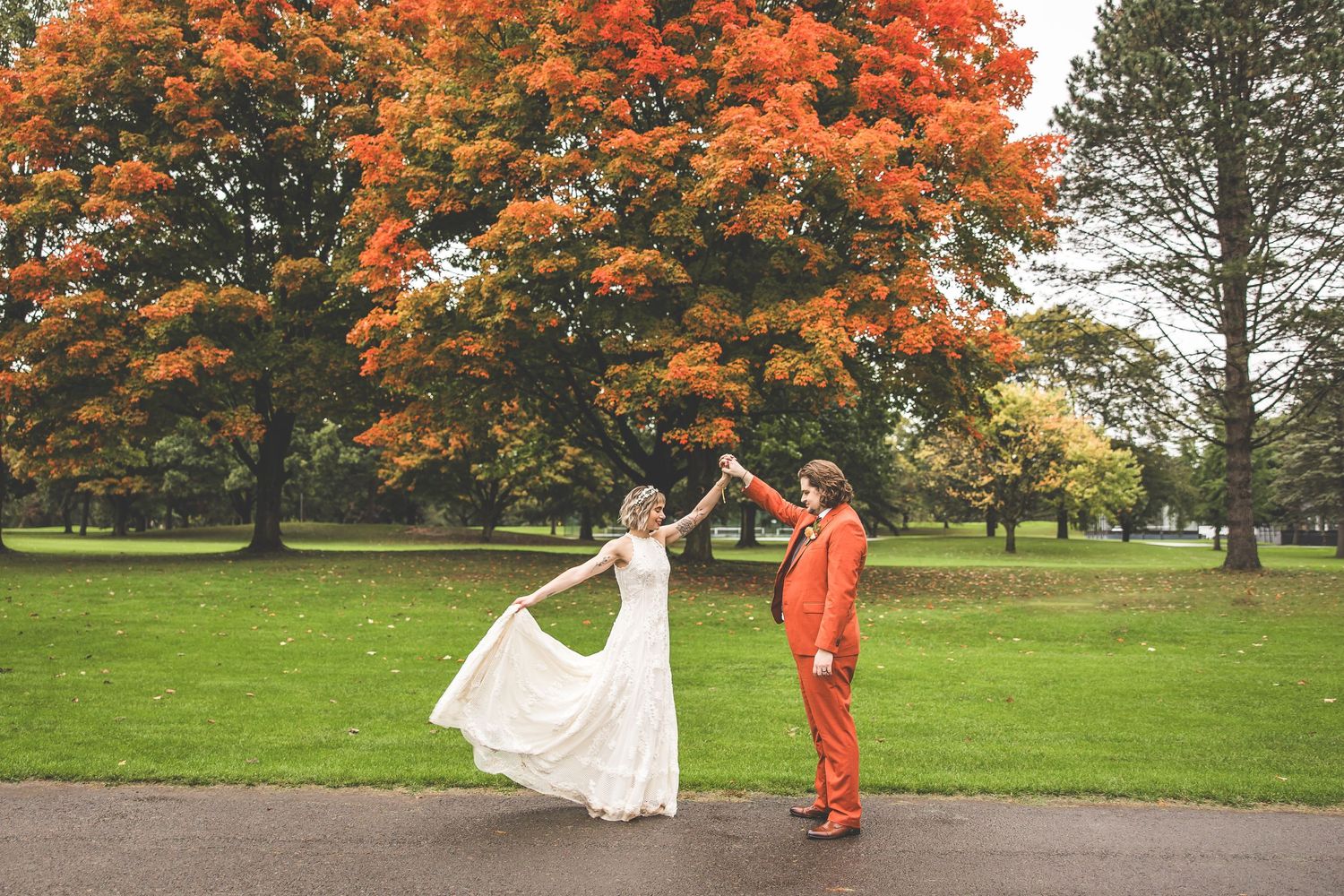 A couple dances and celebrates on their wedding day with autumn trees creating a colorful backdrop.