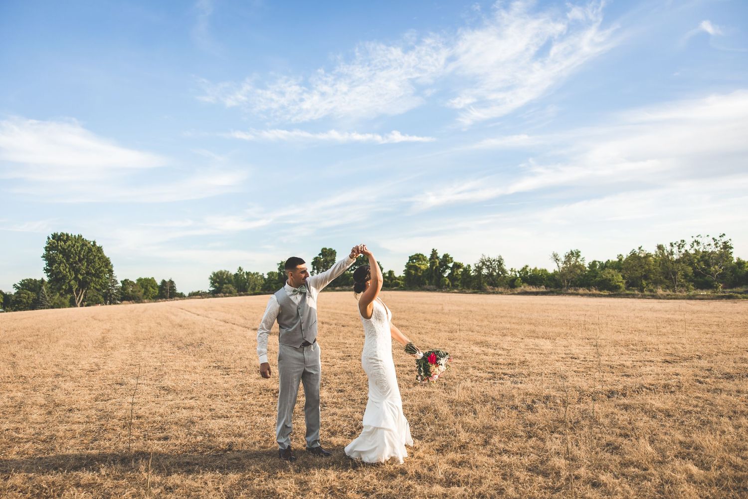 A couple walks hand in hand through a golden wheat field during sunset.
