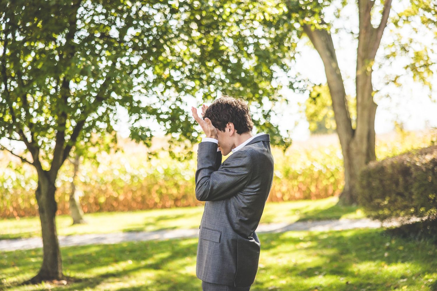 An emotional moment captured during a wedding as a groom reacts in a sunlit garden setting.