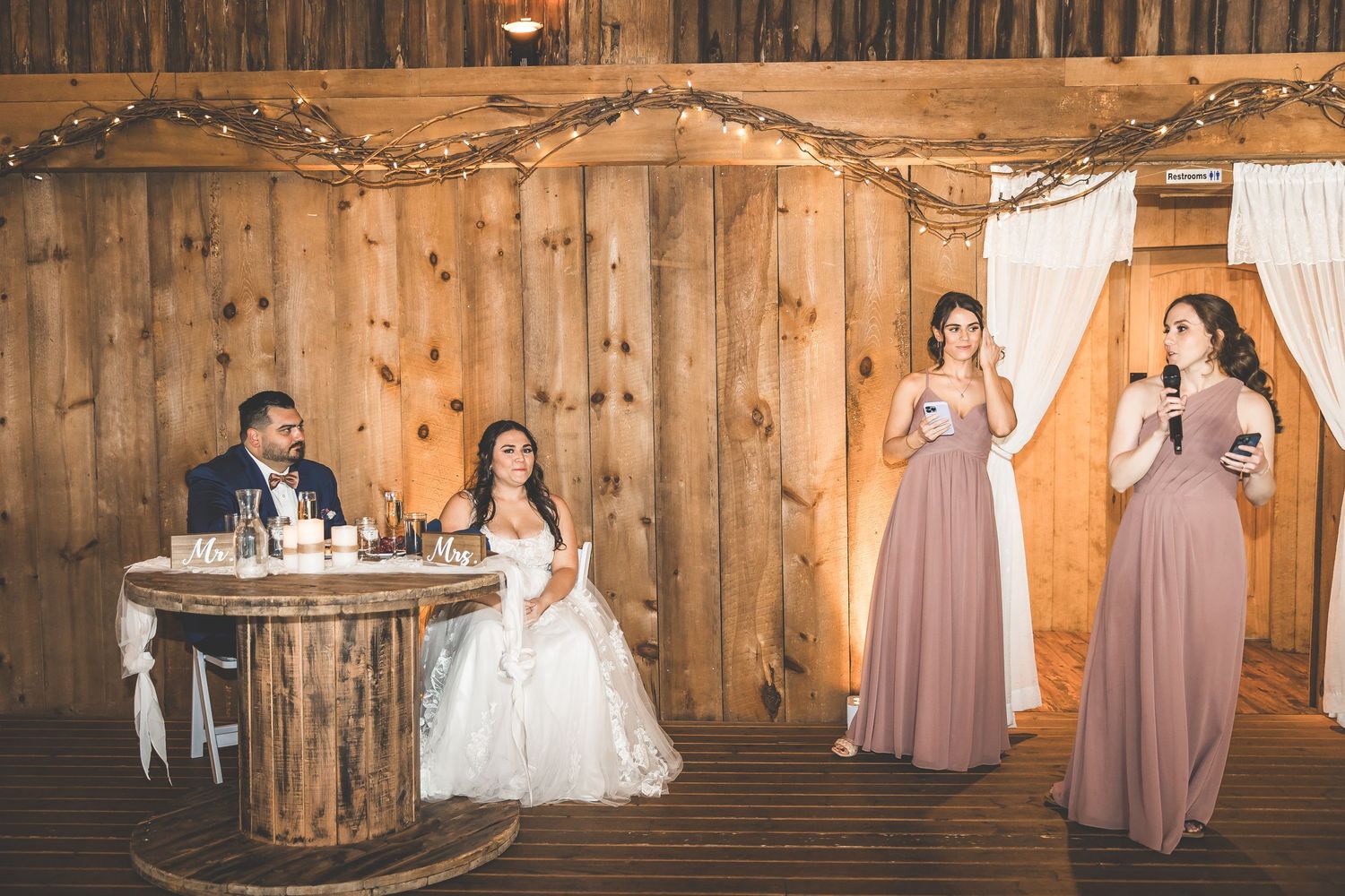 Wedding celebration in a rustic barn decorated with string lights and white draping.