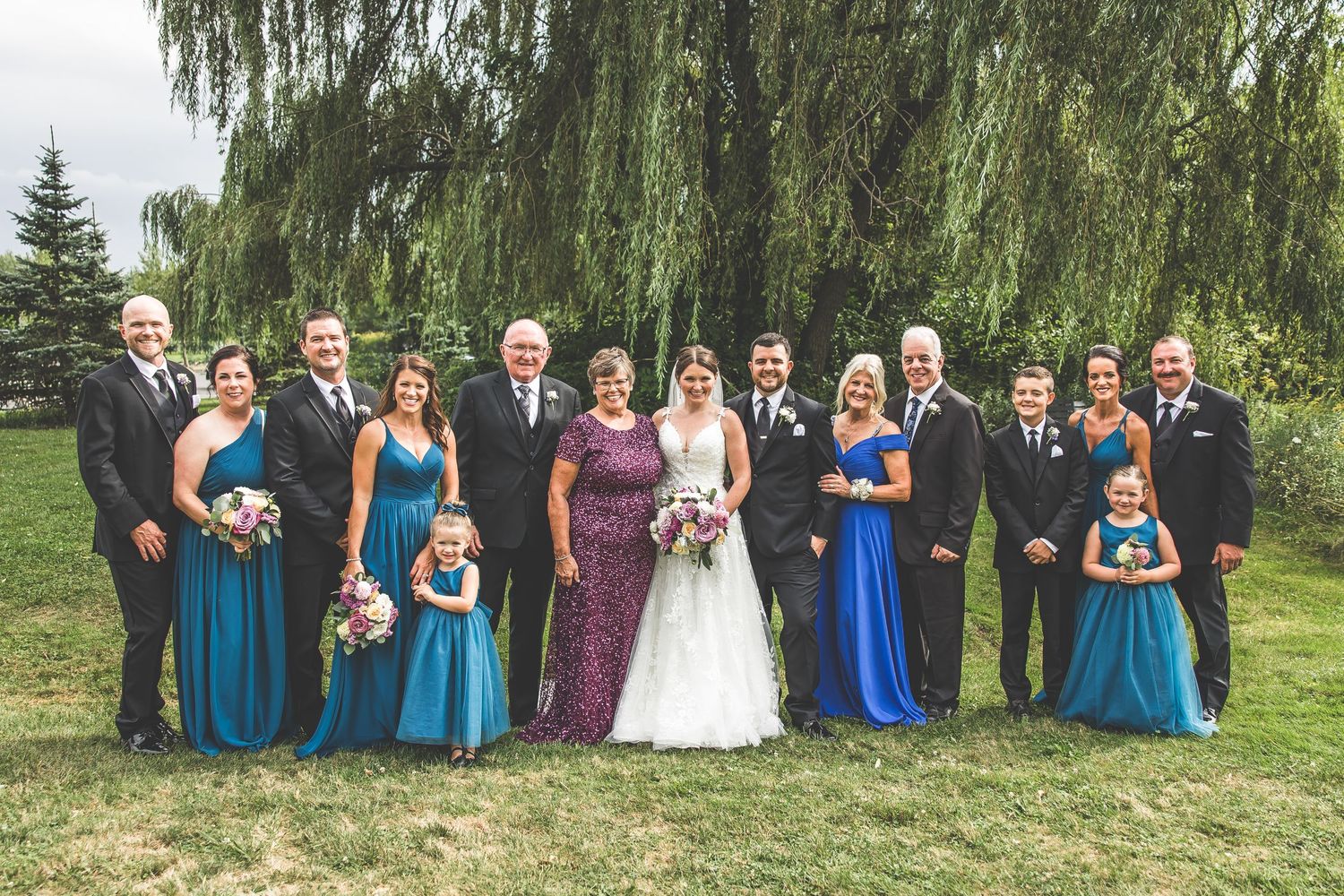 Large wedding party group photo with bridesmaids in blue dresses outdoors.