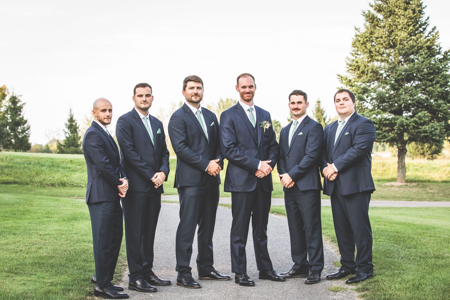 Groomsmen in navy suits pose formally on golf course.