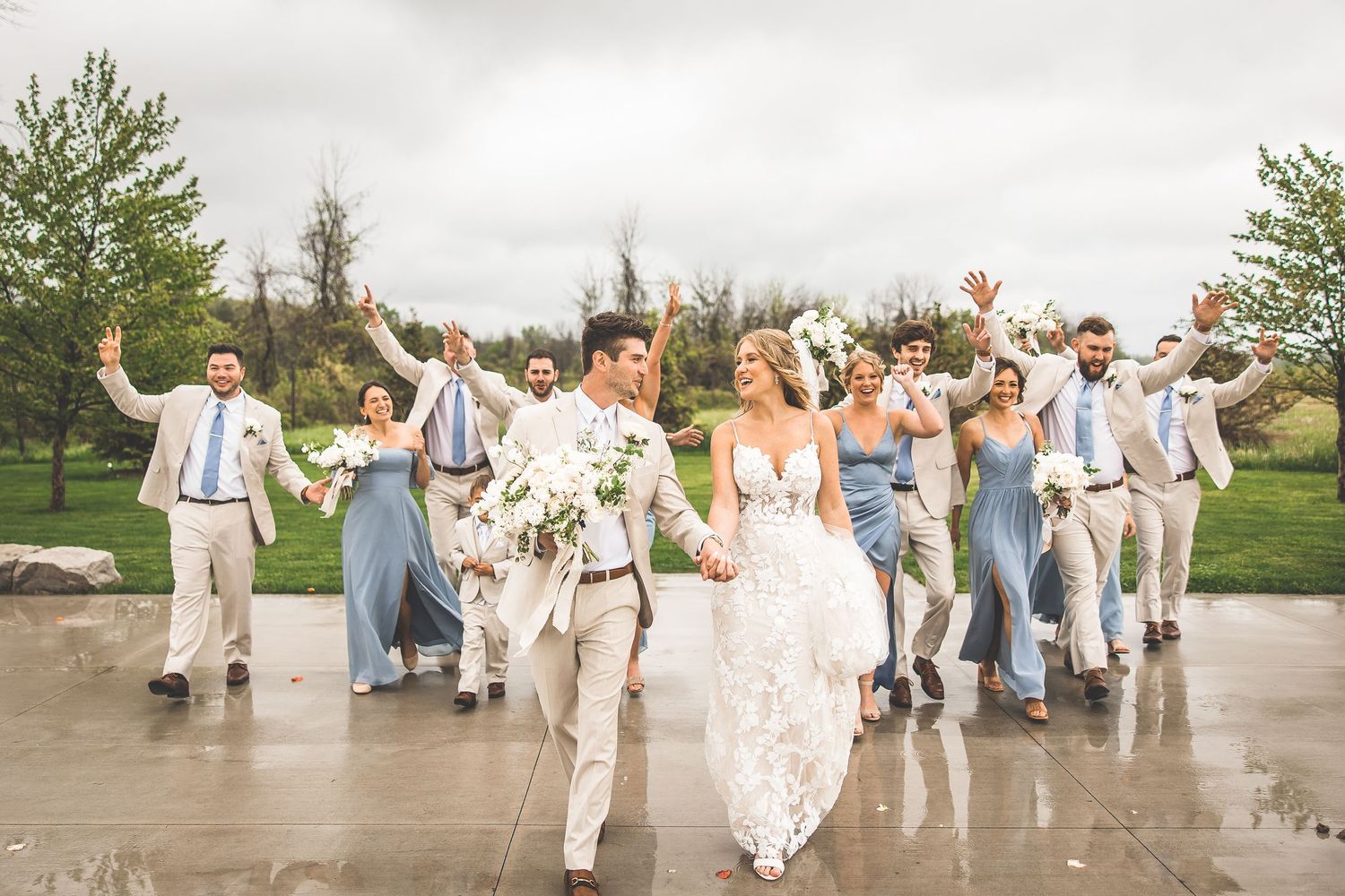 Joyful wedding party celebrating outdoors in light beige and powder blue attire.