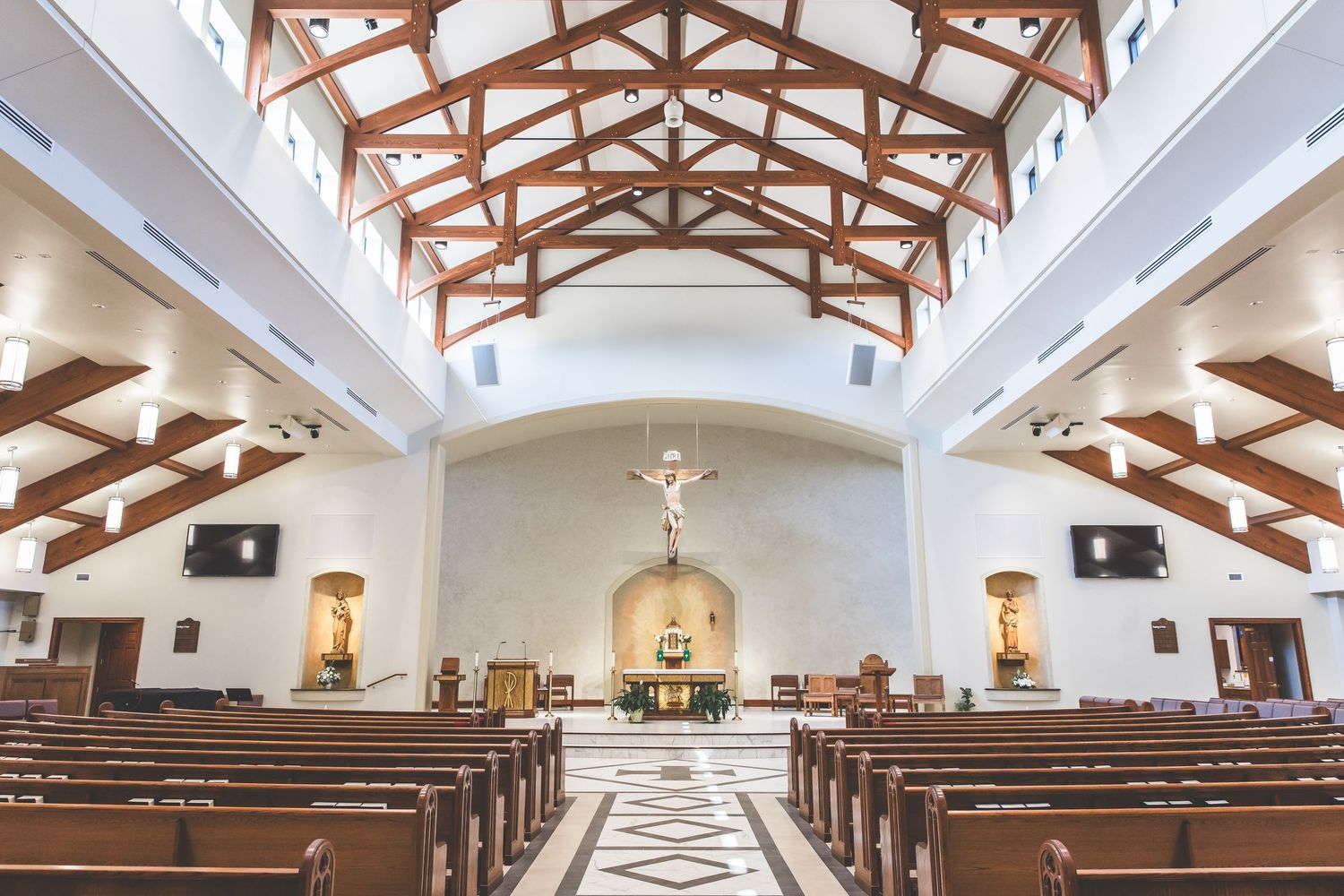 Interior view of a modern church sanctuary with exposed wooden beams and white vaulted ceilings.
