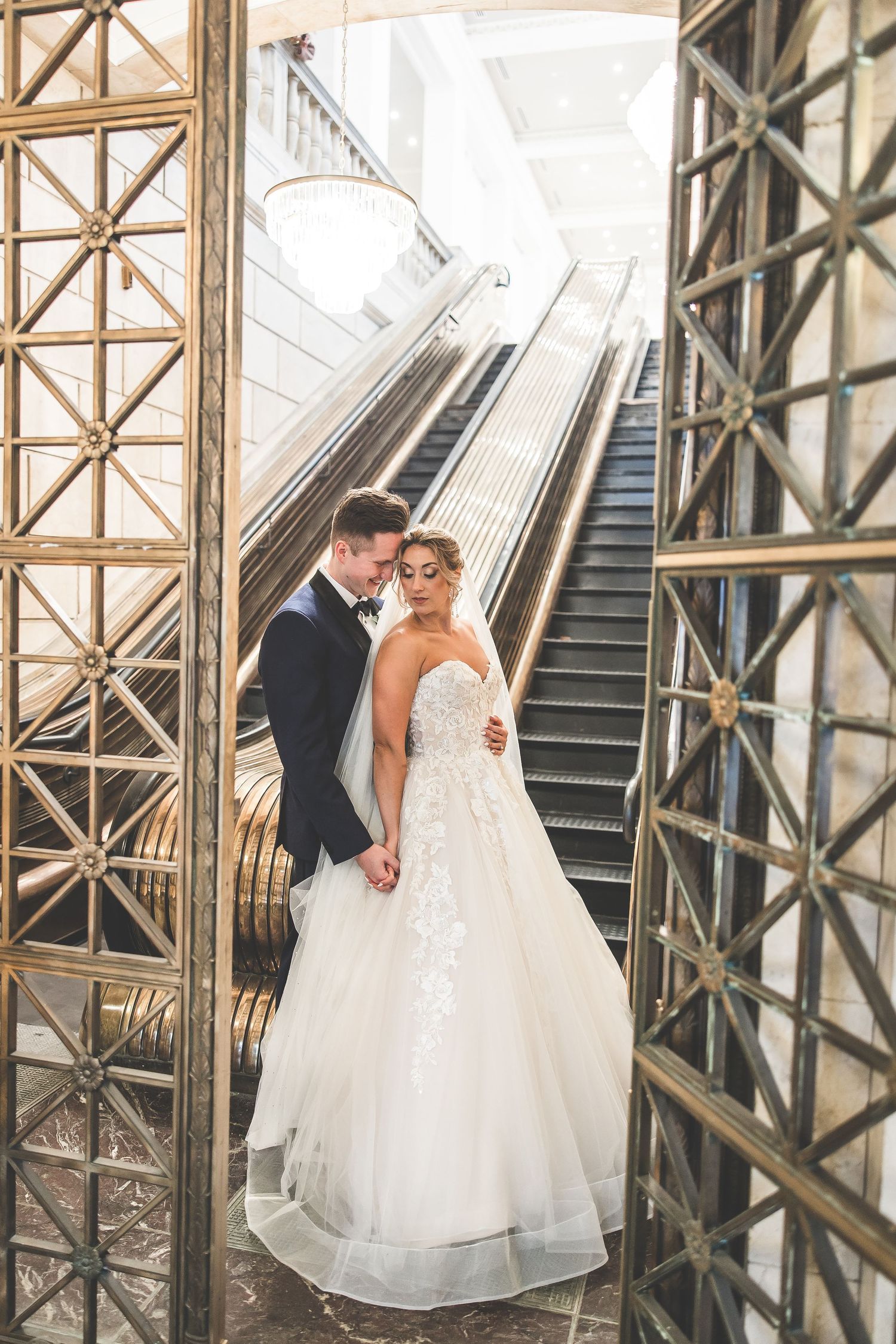 Wedding couple posing on art deco staircase with geometric gold details.