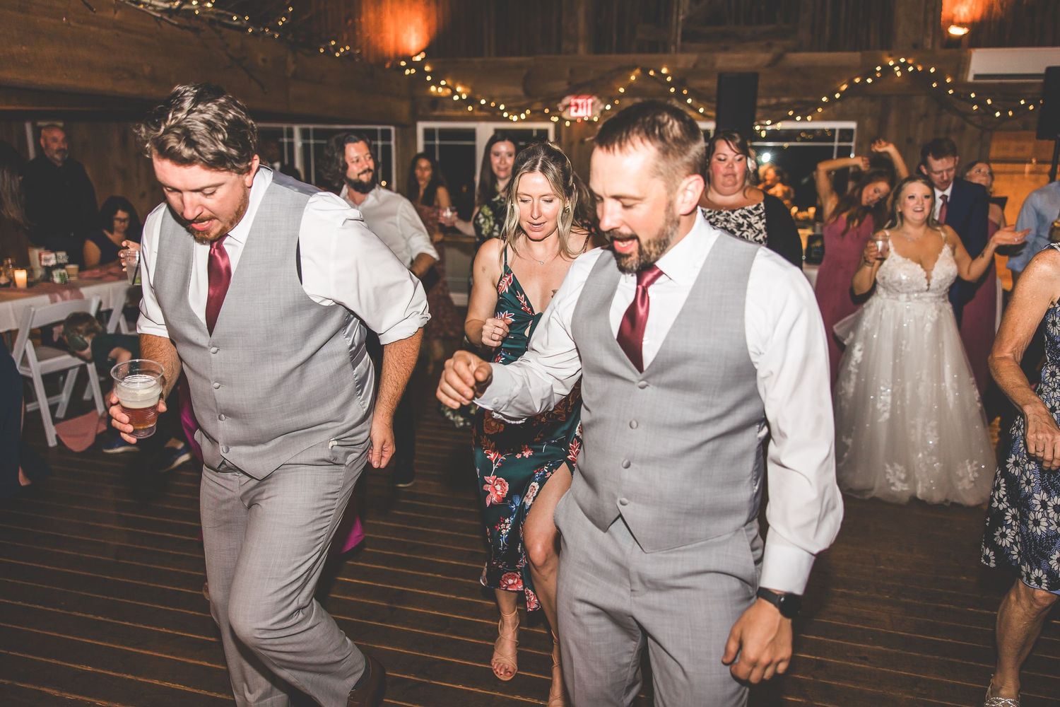 Guests in formal attire dance and celebrate on a wooden dance floor at a wedding reception.