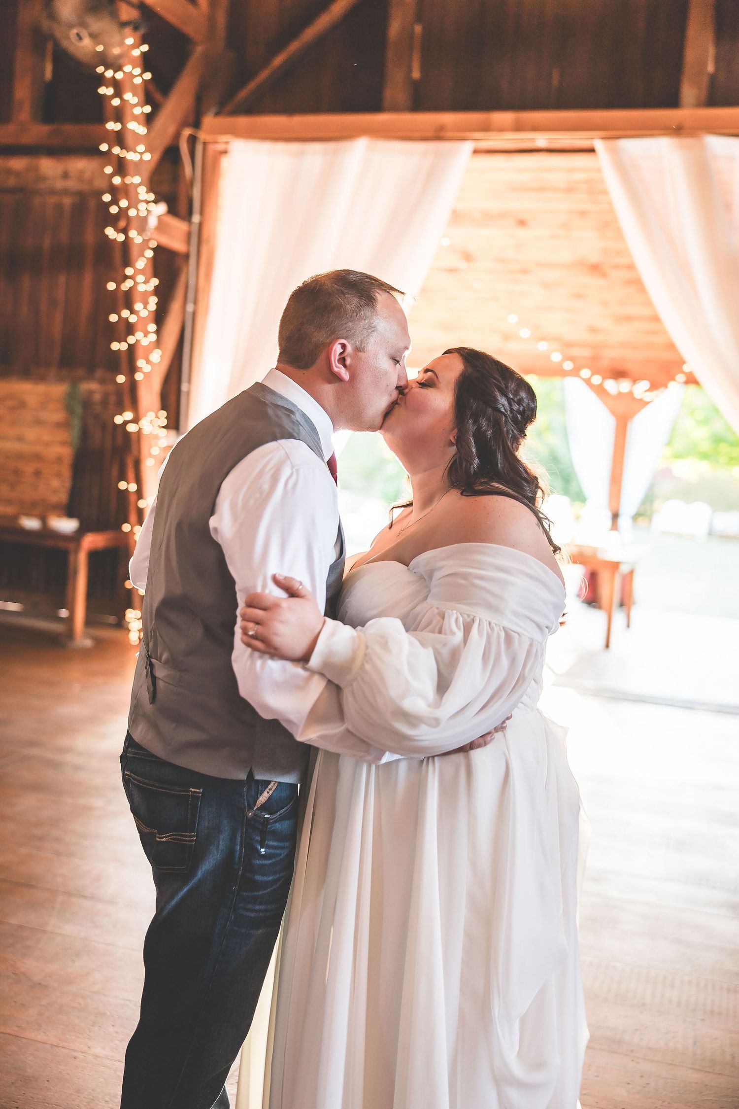 Romantic first dance moment in a rustic barn venue with string lights and white draping.