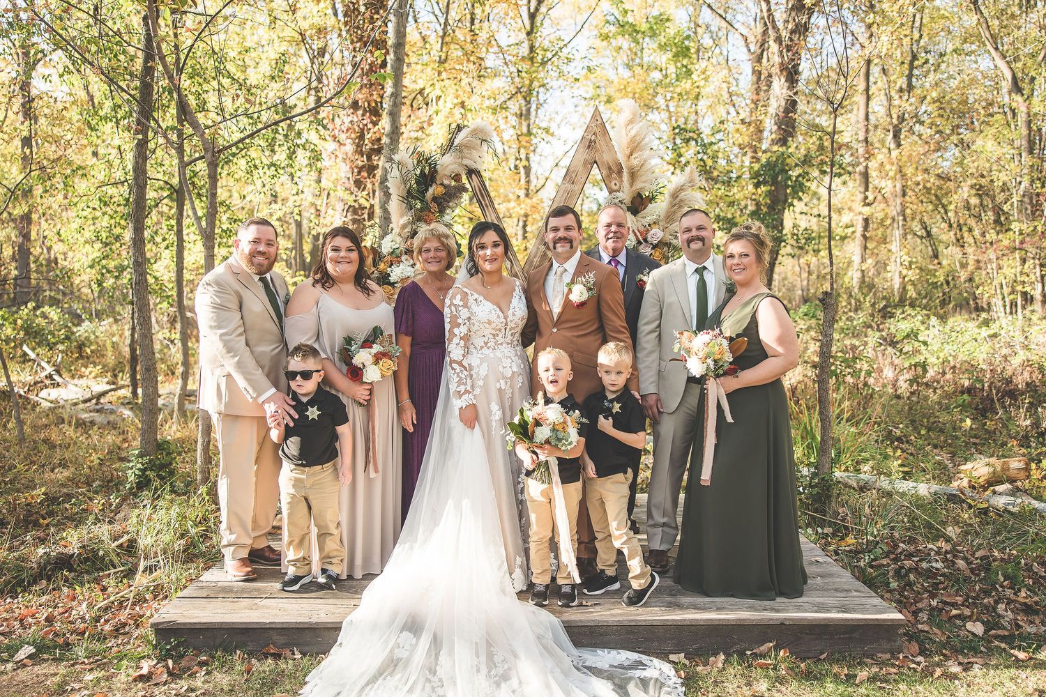 Large wedding party gathered in a forest setting with autumn colors and natural lighting.