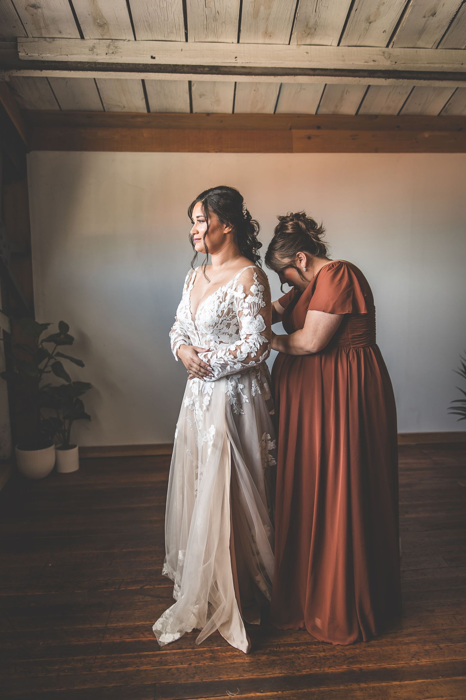 Final wedding dress adjustments being made in room with wooden ceiling and natural light.