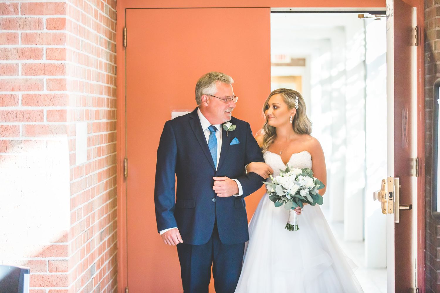 Wedding couple in a brick hallway with orange walls and natural lighting.