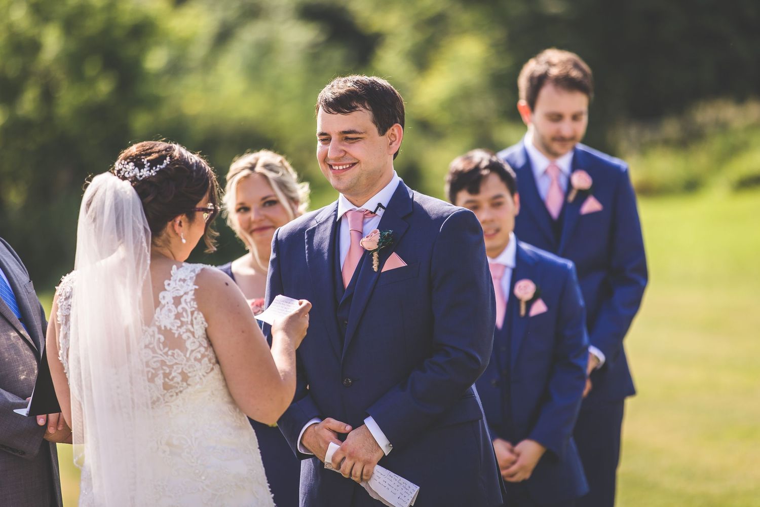 Wedding party in navy suits and formal attire gathered during outdoor ceremony.