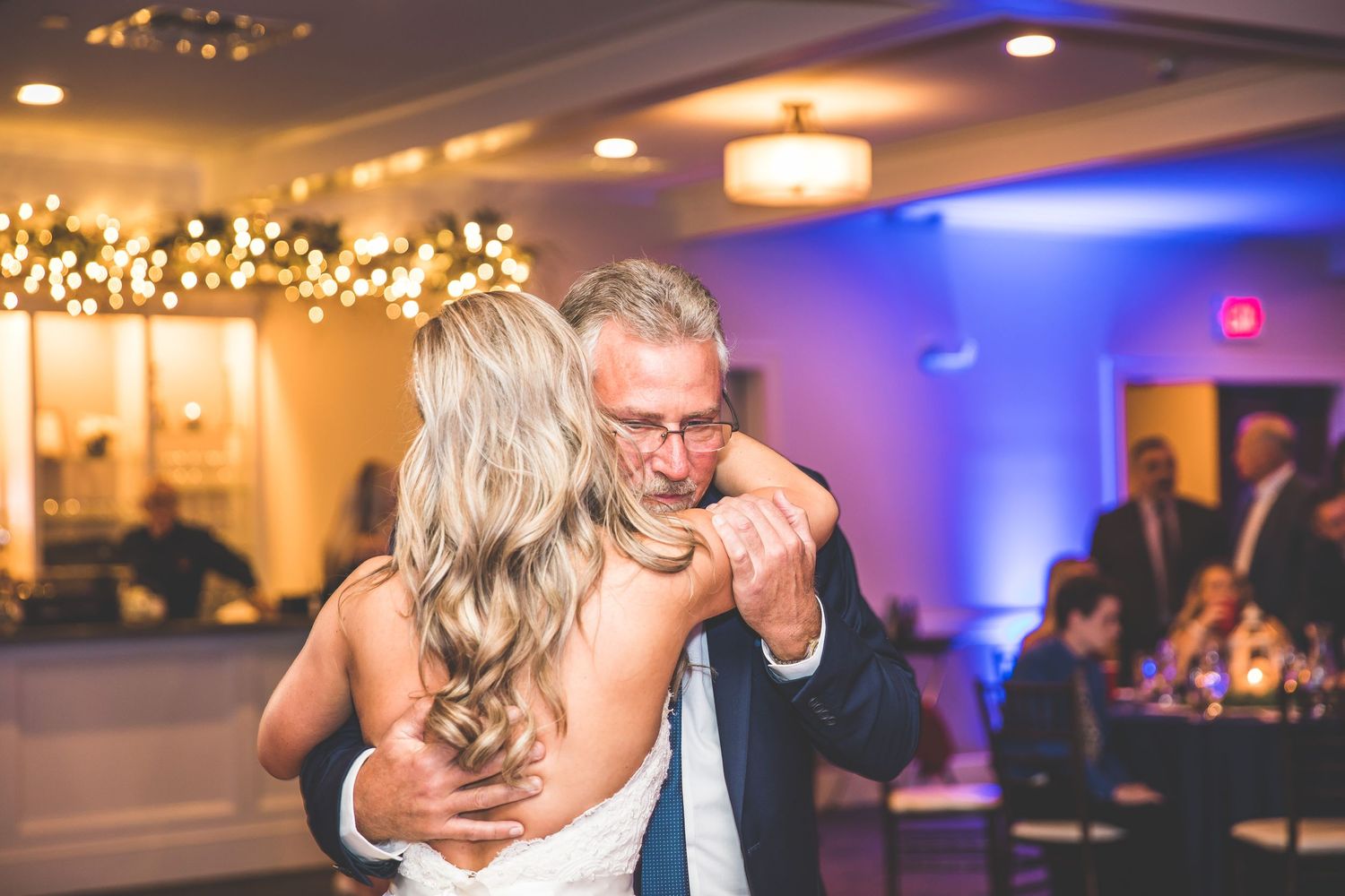 Intimate father-daughter dance moment captured at wedding reception with blue ambient lighting.
