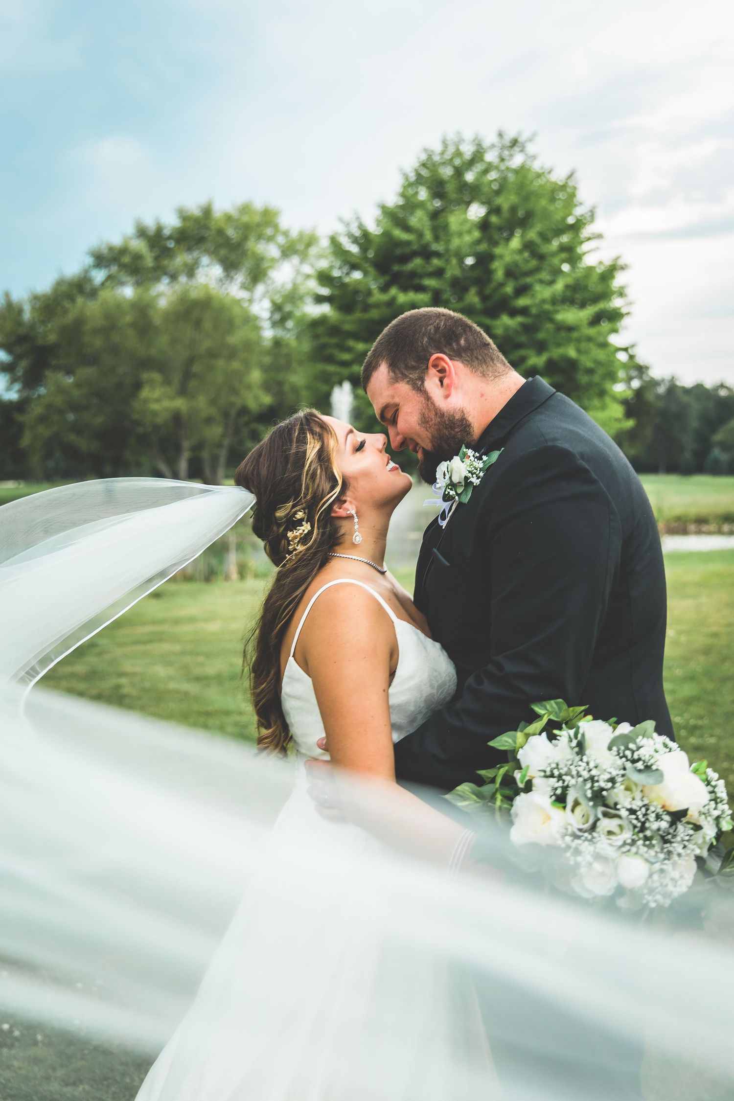 Flowing white veil creates romantic wedding portrait in outdoor setting.