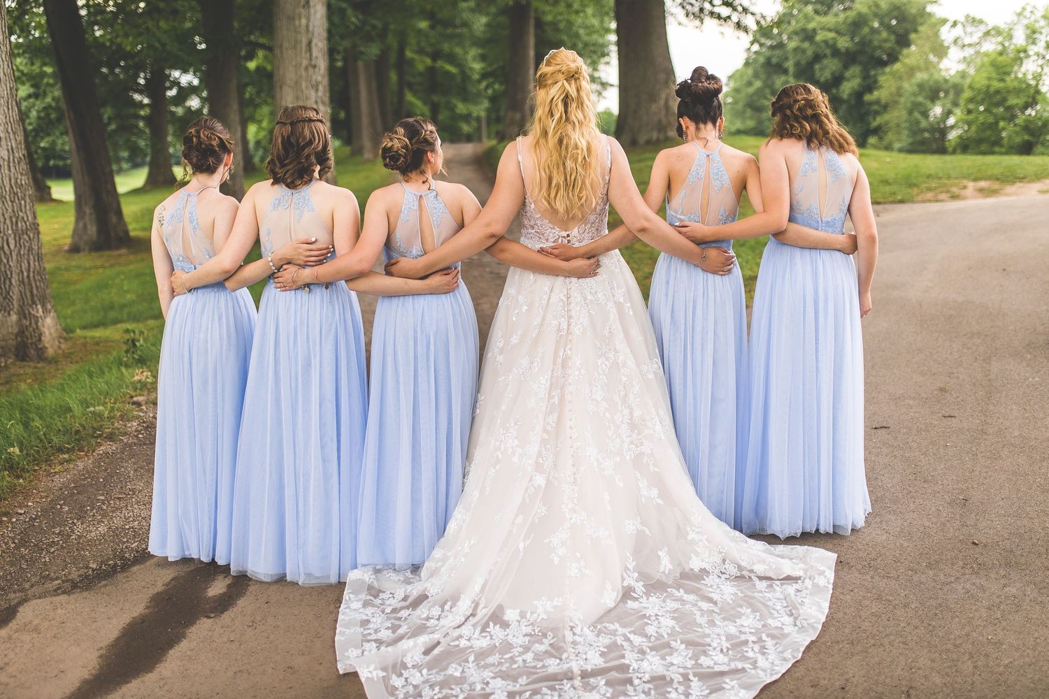 Bride and bridesmaids in light blue dresses stand together showing the wedding gown's train.