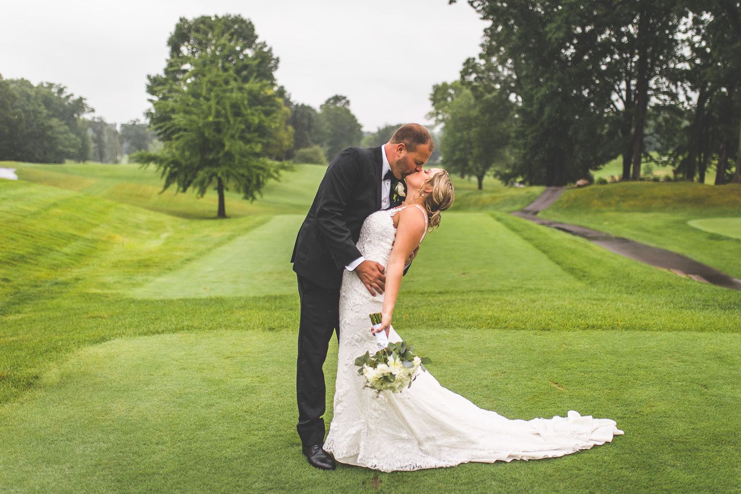 Newlyweds walk hand in hand across scenic golf course landscape.