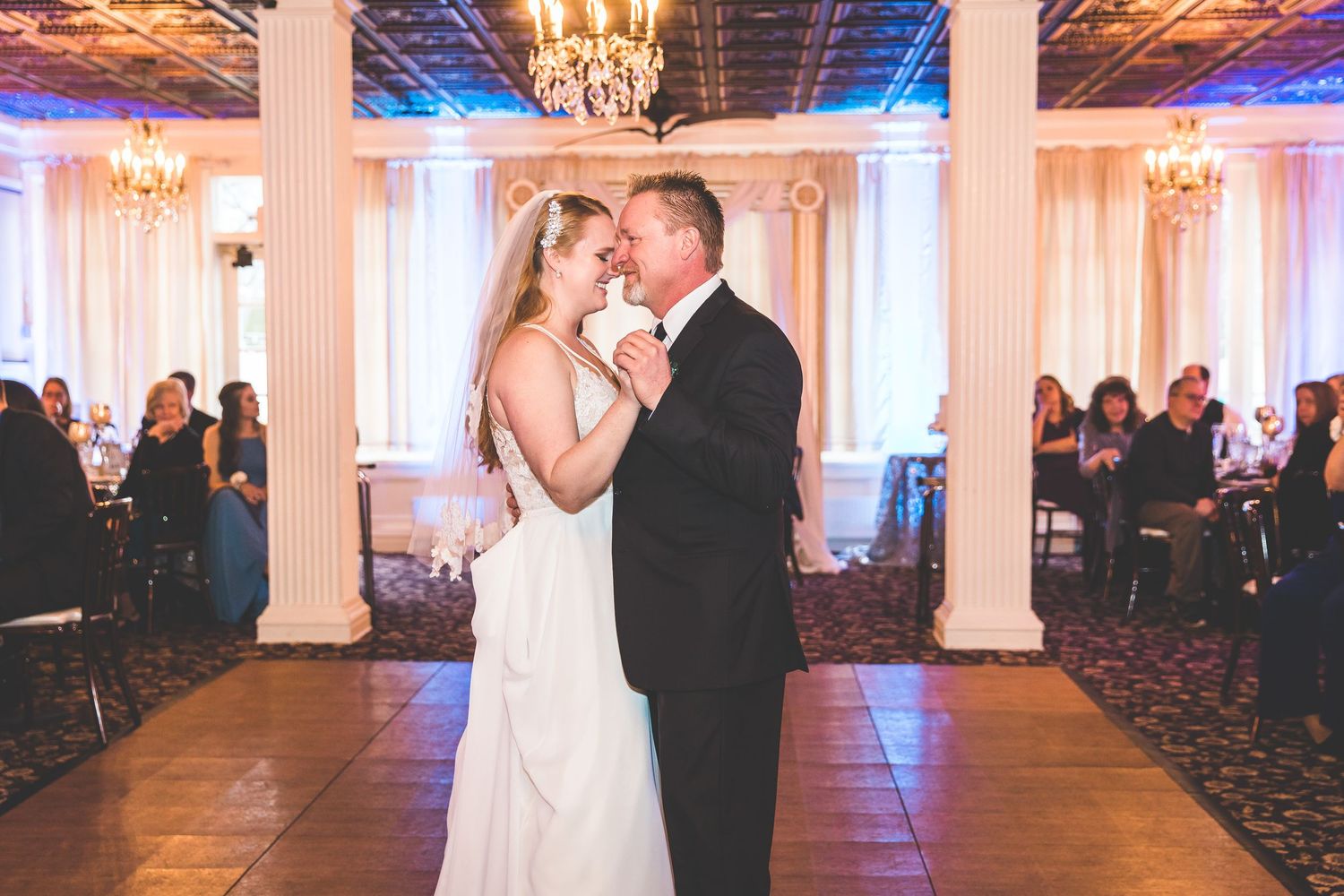 Elegant wedding reception venue with crystal chandeliers and white columns in a grand ballroom.