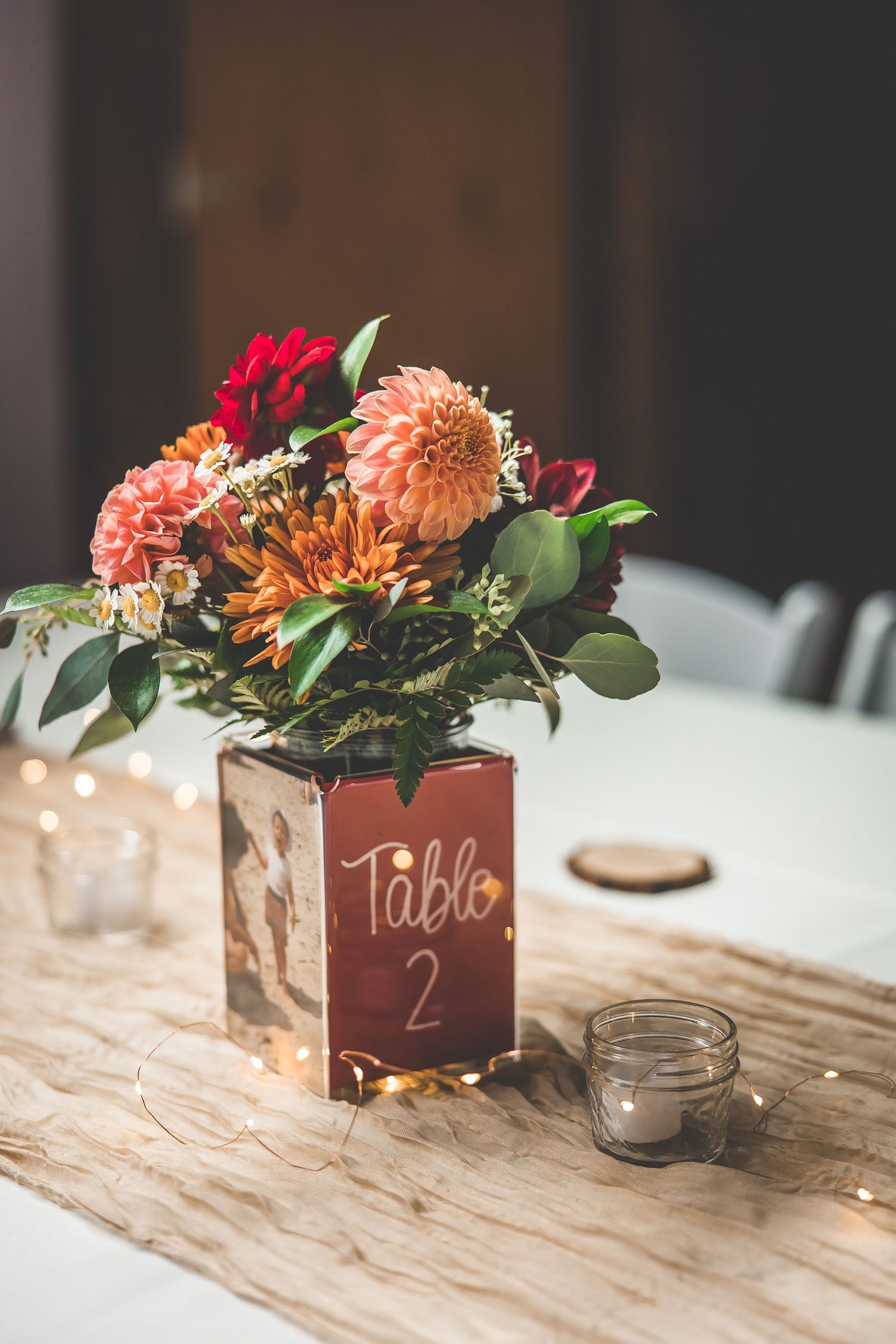 Rustic wooden table centerpieces feature coral dahlias and table numbers for wedding reception.