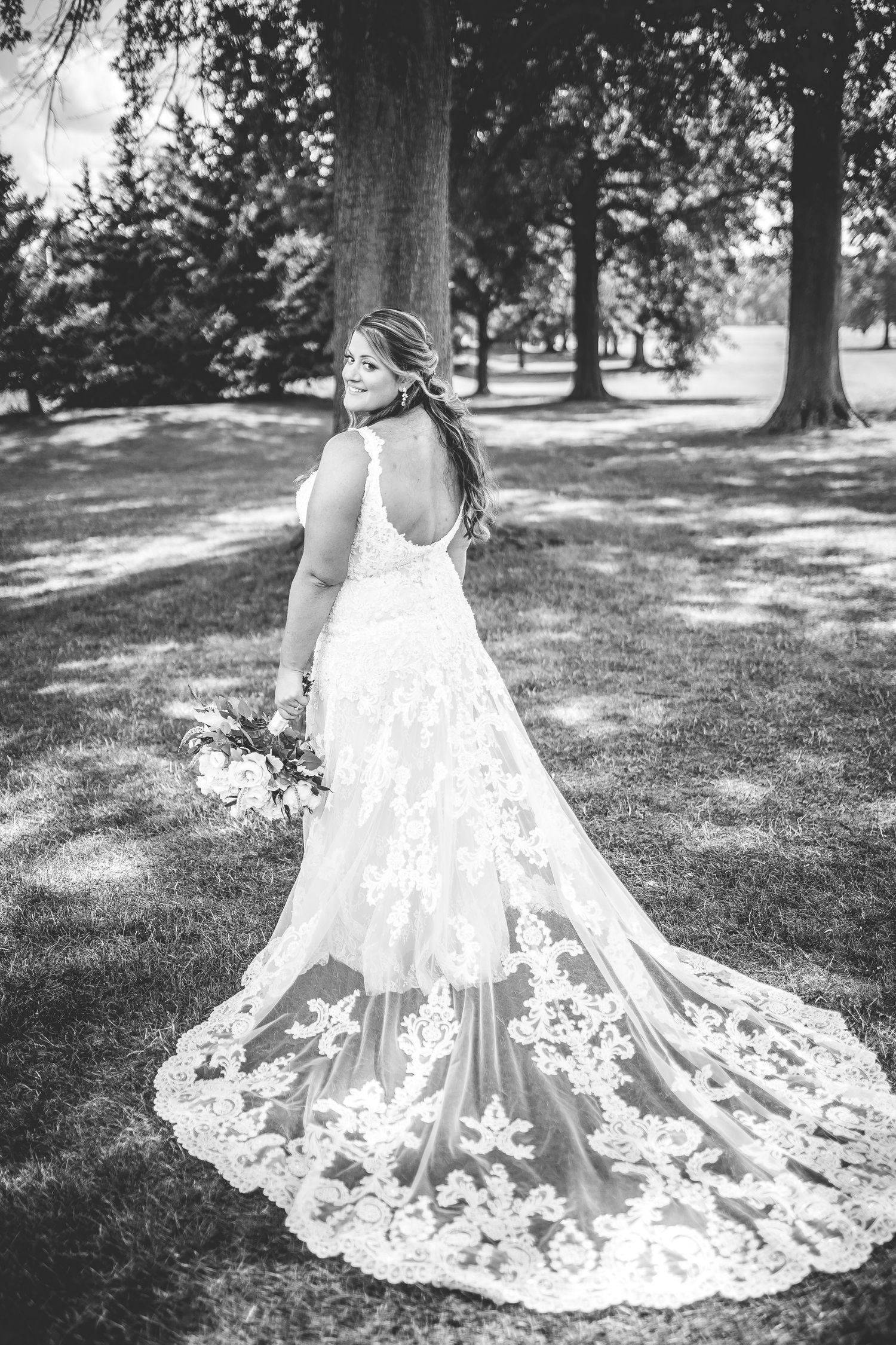 Detailed lace train of a white wedding dress spread out on green grass in a garden setting.