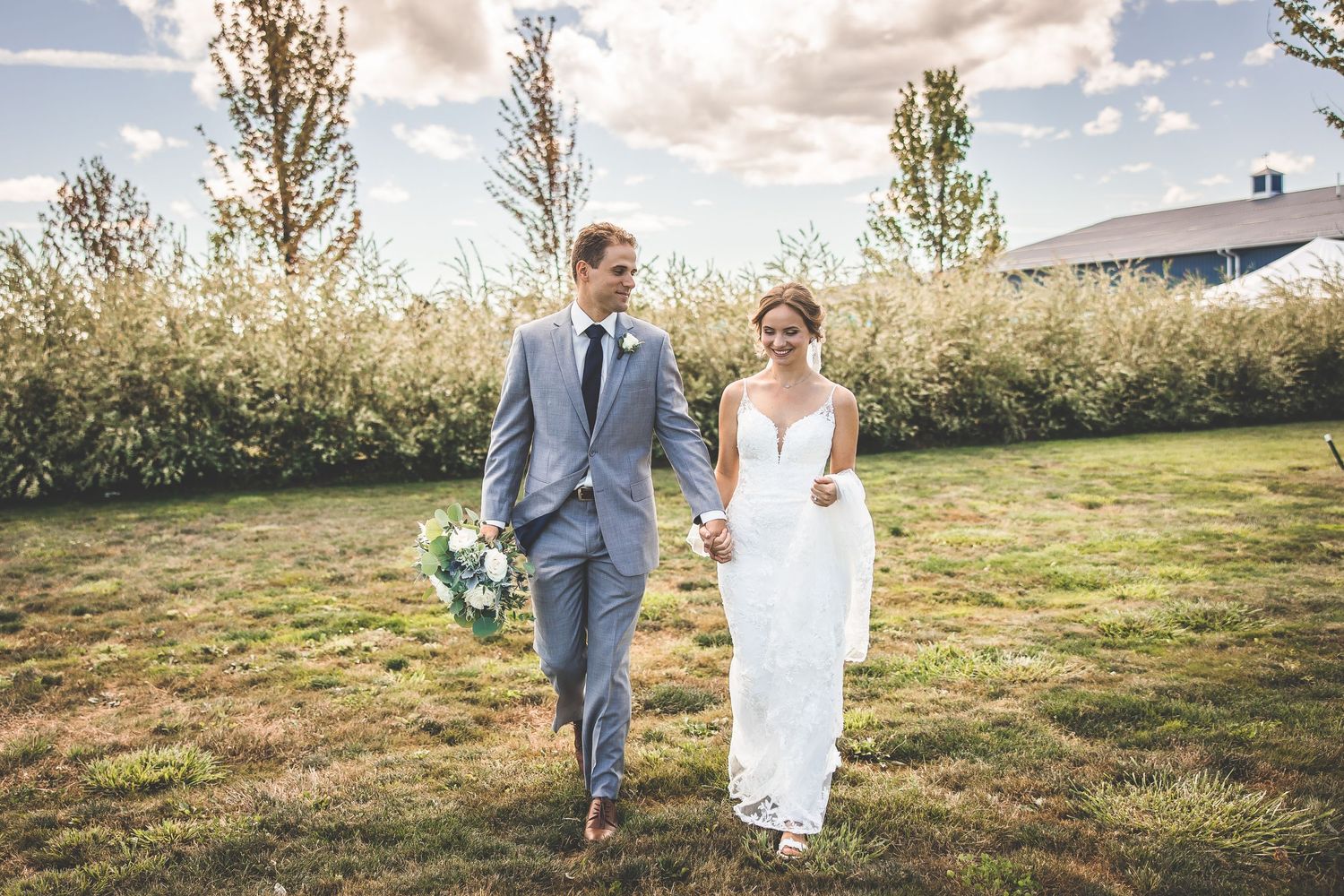 Couple walking together through a scenic outdoor field during a wedding photoshoot.