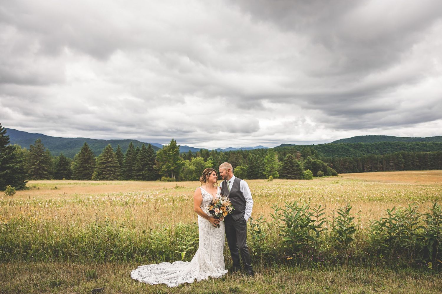 Newlyweds pose together against a backdrop of mountains and cloudy skies.