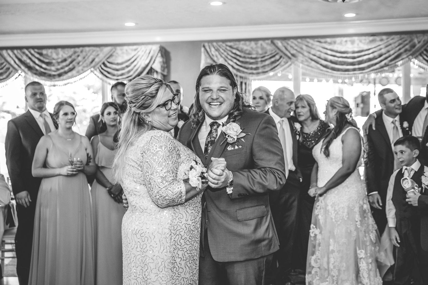 Wedding reception guests celebrate and dance in an elegant ballroom setting.
