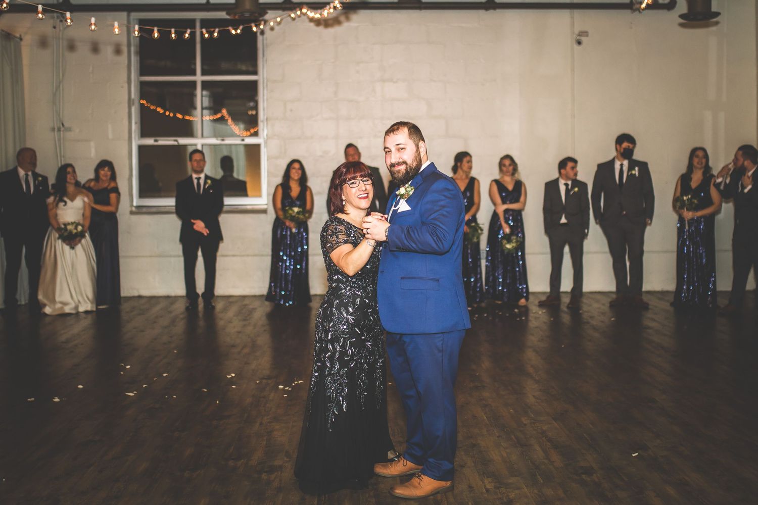 Wide shot of wedding reception venue with guests lining the walls and couples dancing.