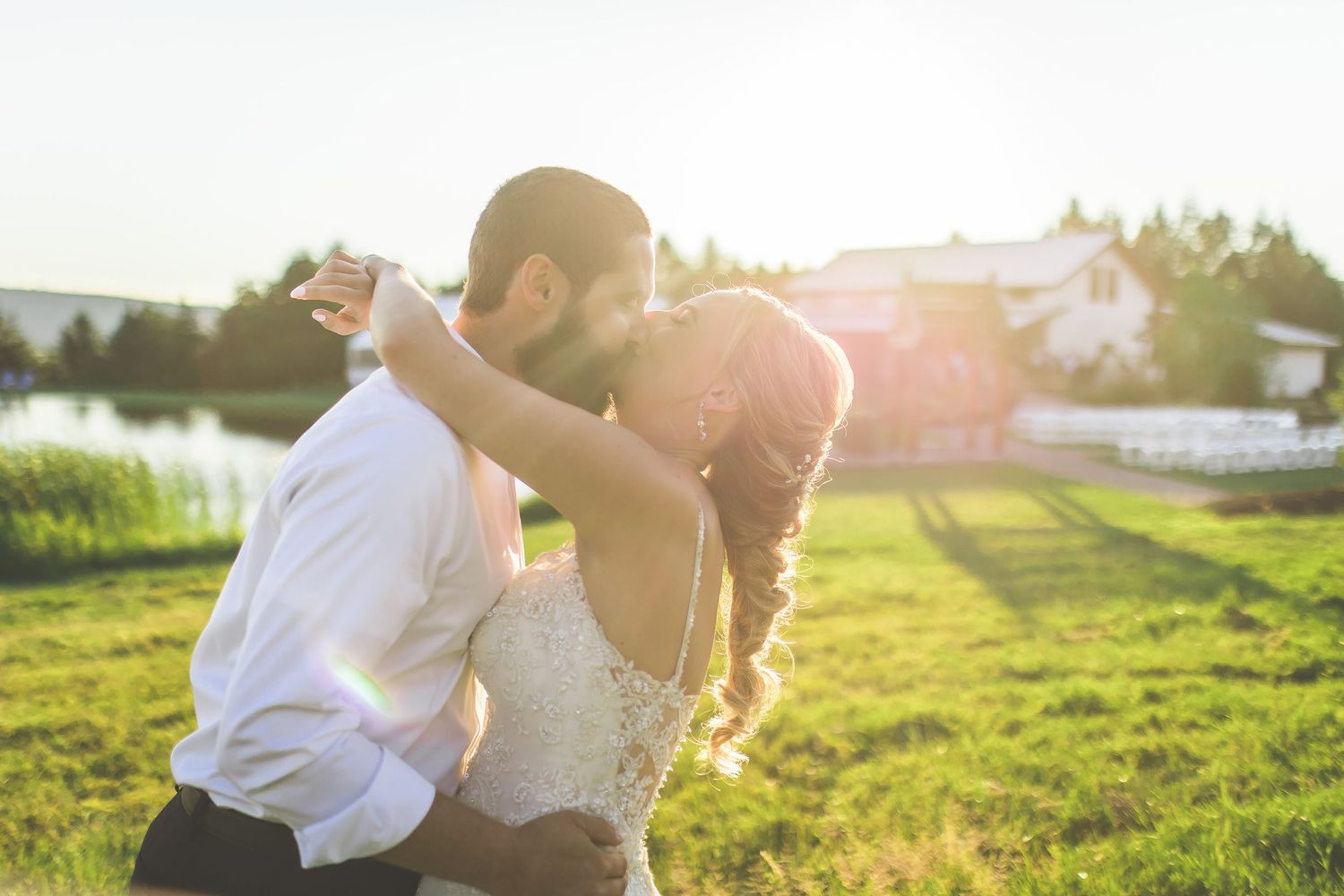 Golden hour portrait of couple dancing in a sunlit field near a farmhouse.