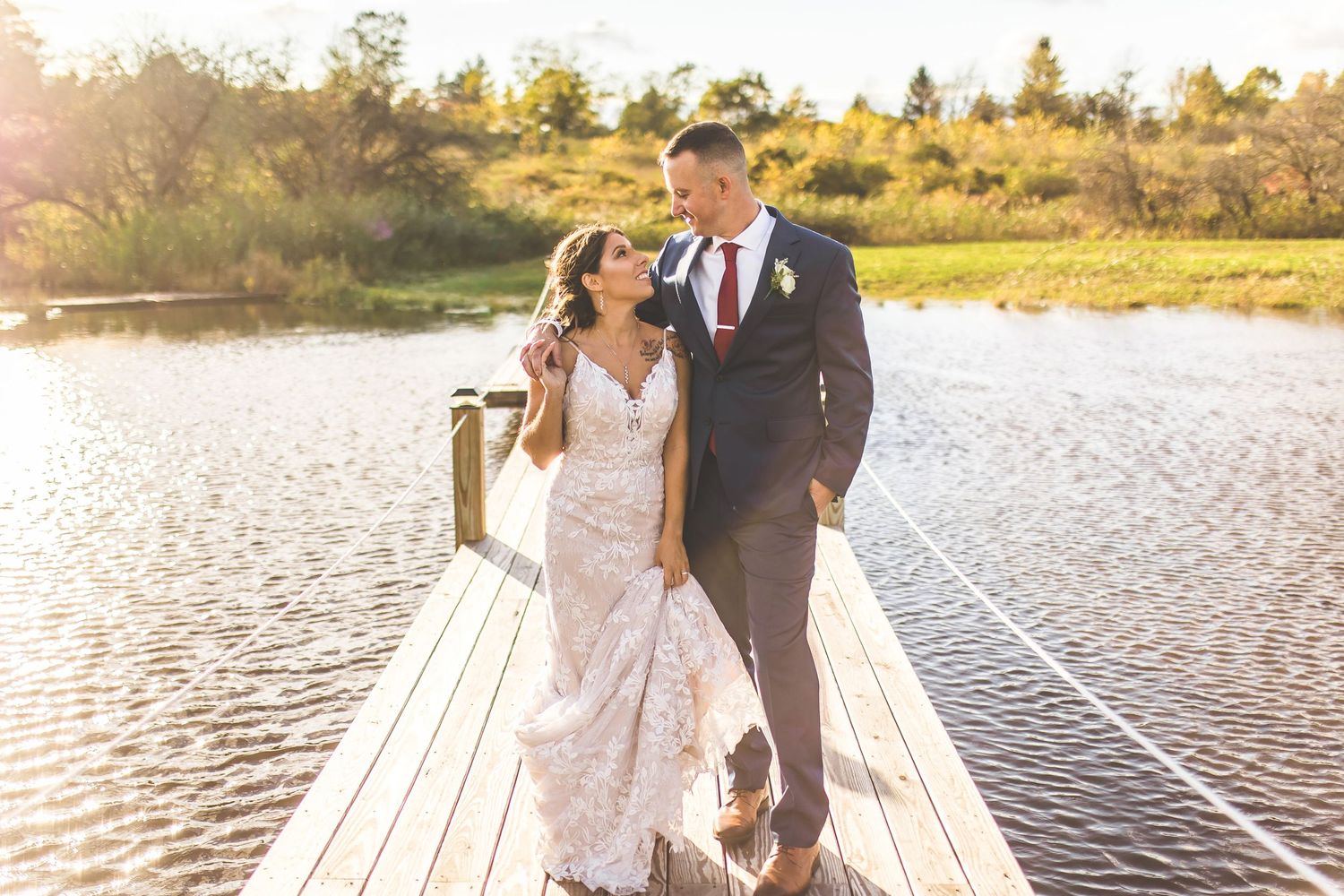Wedding couple enjoys sunset photos on rustic dock overlooking serene lake.