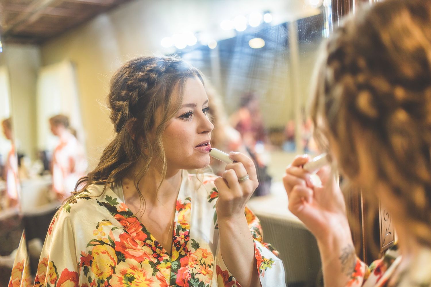 Getting ready scene with floral robes while applying makeup in a bridal preparation room.