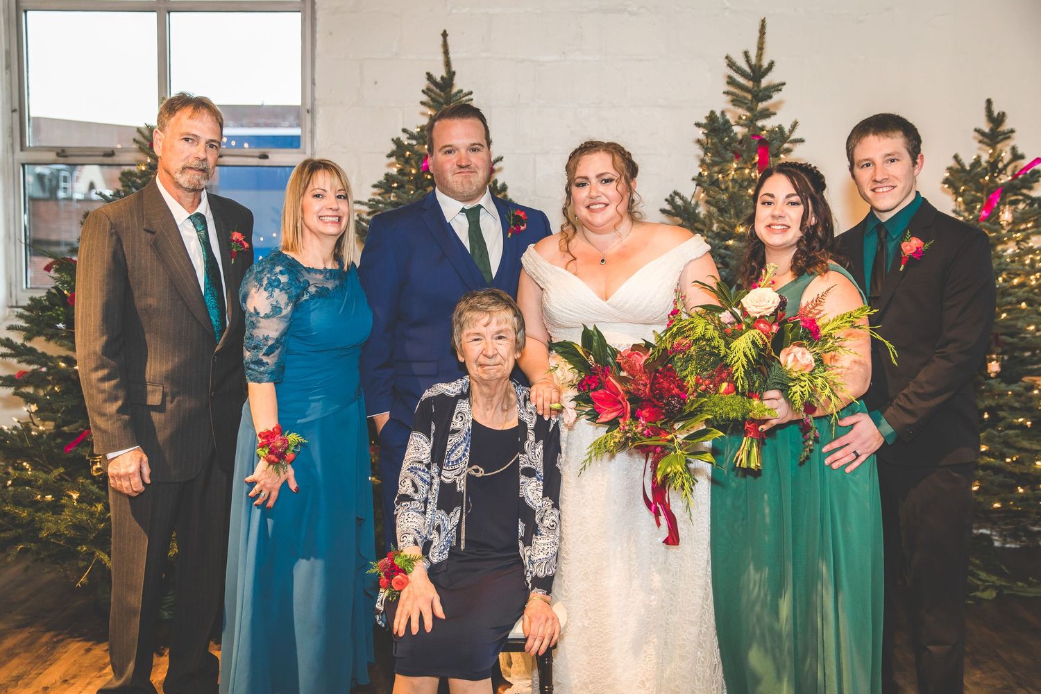Family group portrait in front of Christmas trees at winter wedding celebration.