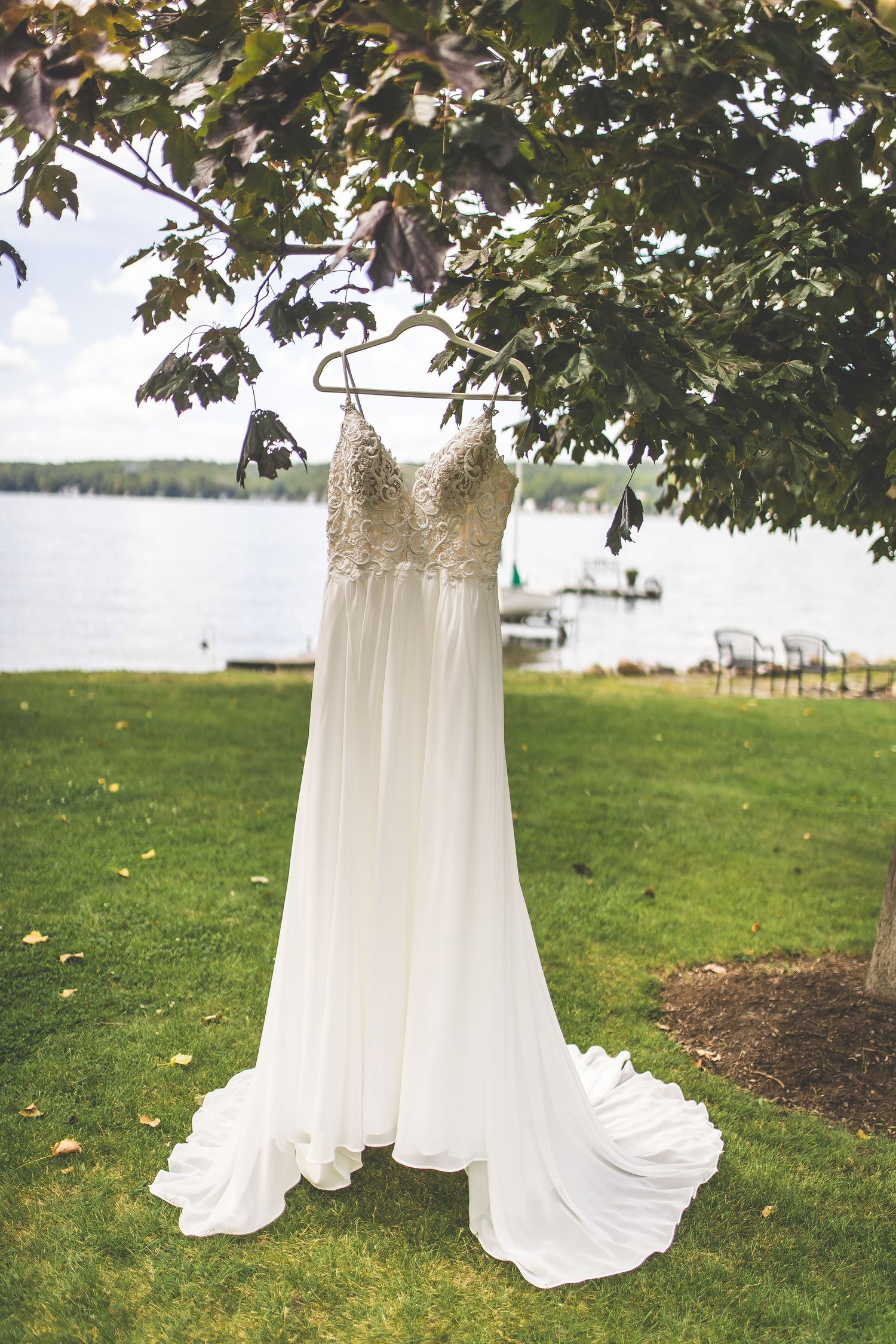 White flowing wedding dress hanging from tree branches with lake view in background.