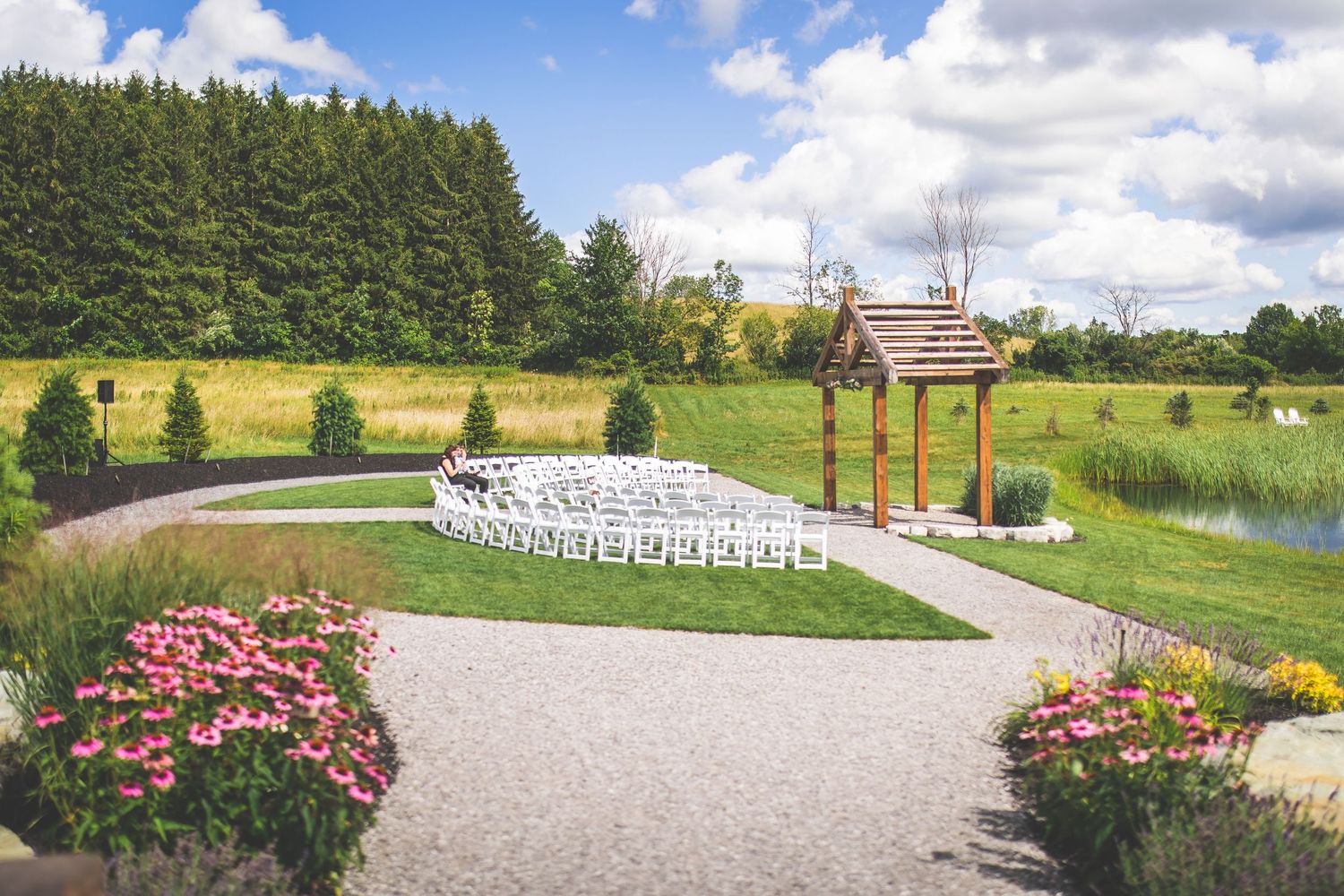 Panoramic view of an outdoor wedding venue with white chairs and floral garden landscaping.
