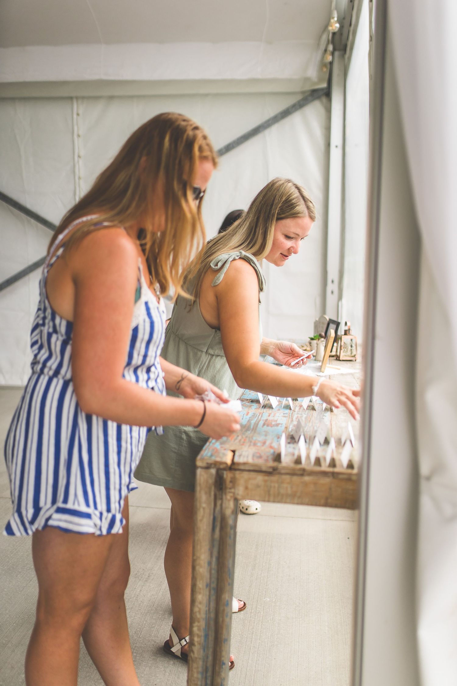 Women in striped tops looking at wedding decorations in a white tent.