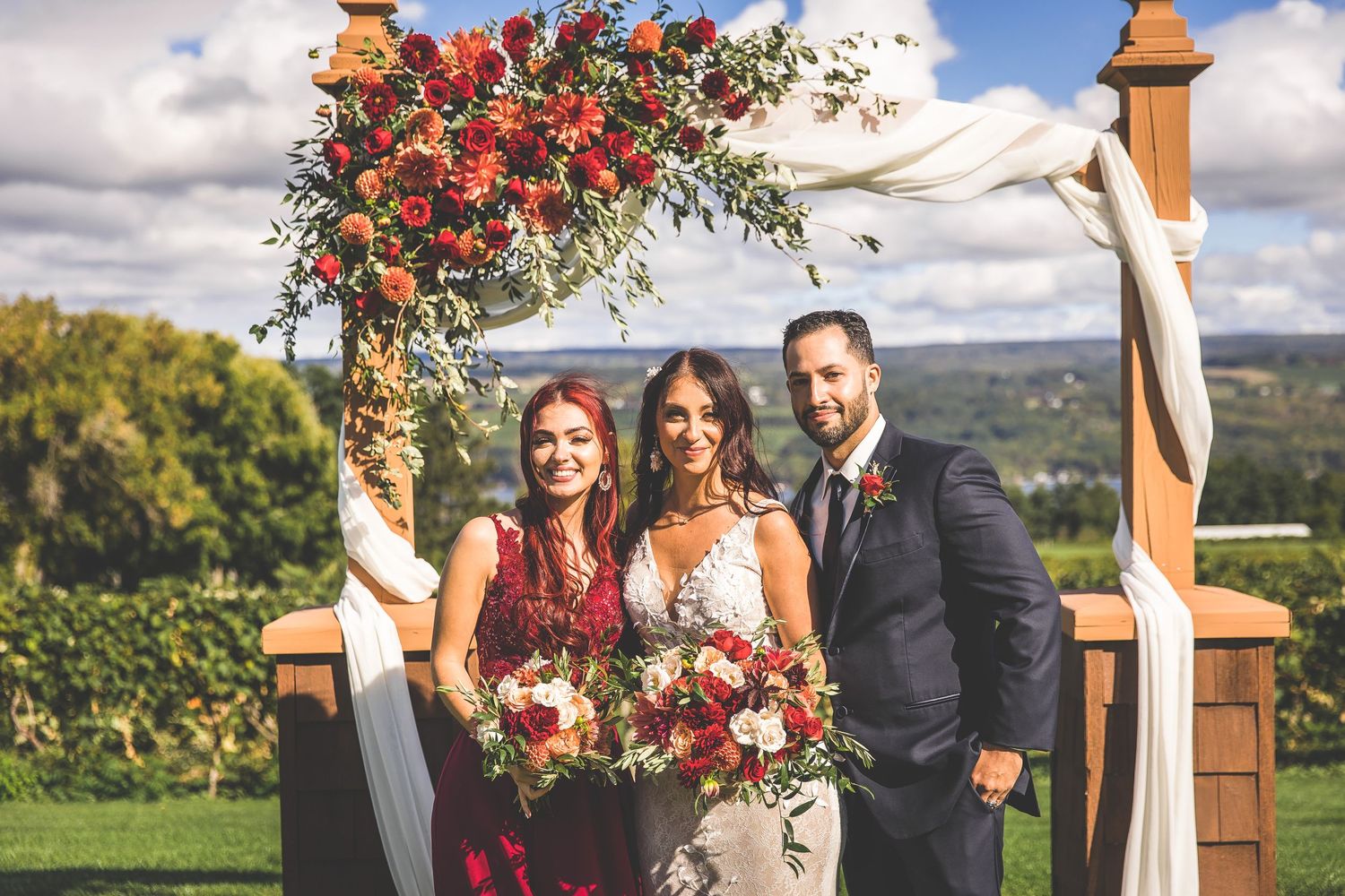 Wedding arch decorated with vibrant red and orange flowers against a blue sky.