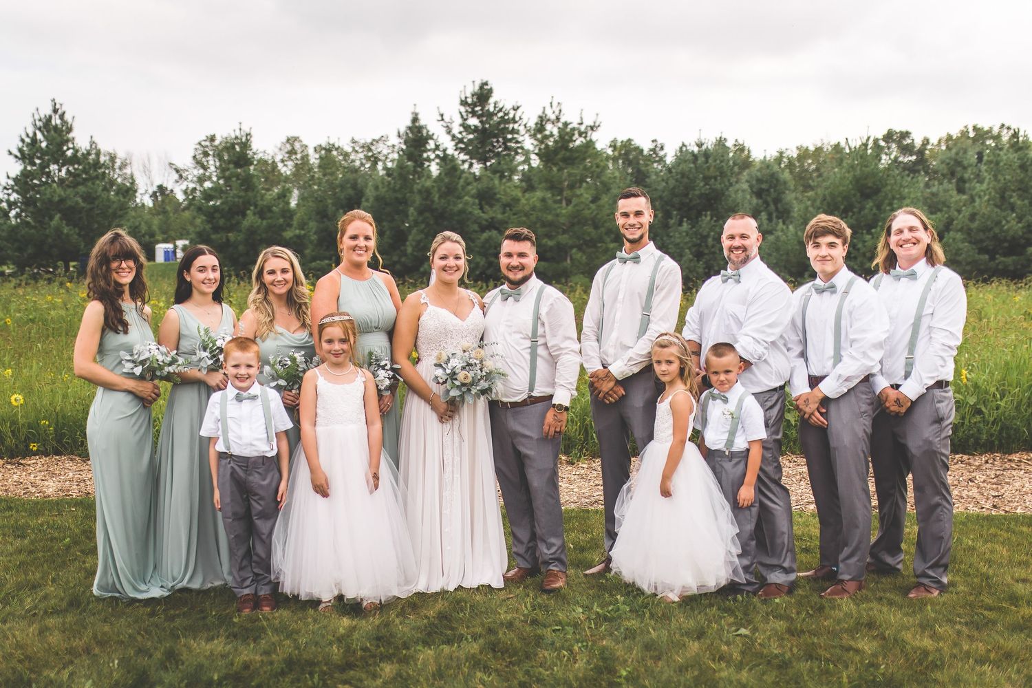 Group photo of wedding party members wearing coordinated pastels and neutrals in a field setting.