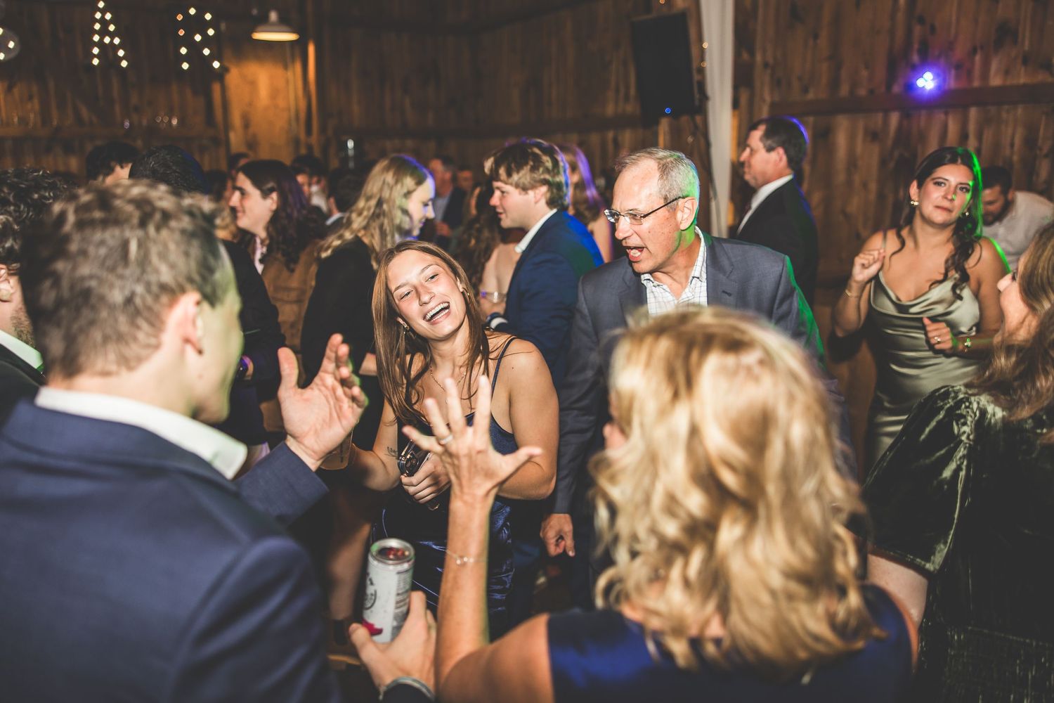 Wedding guests dancing and celebrating under string lights in rustic barn venue.