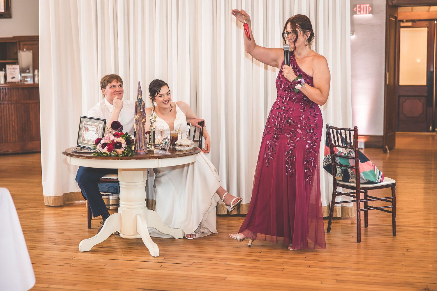 Guests celebrate at an elegant wedding reception with burgundy accents and white draping.