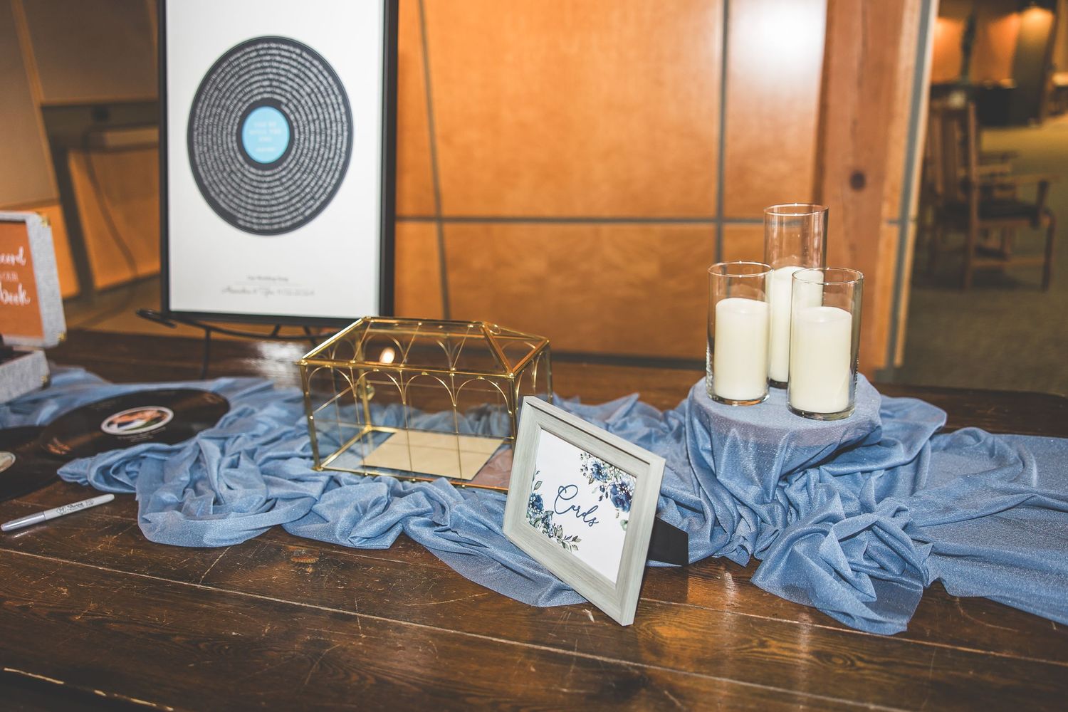 Wedding decor display featuring vinyl record art, candles, and blue fabric on wooden table.