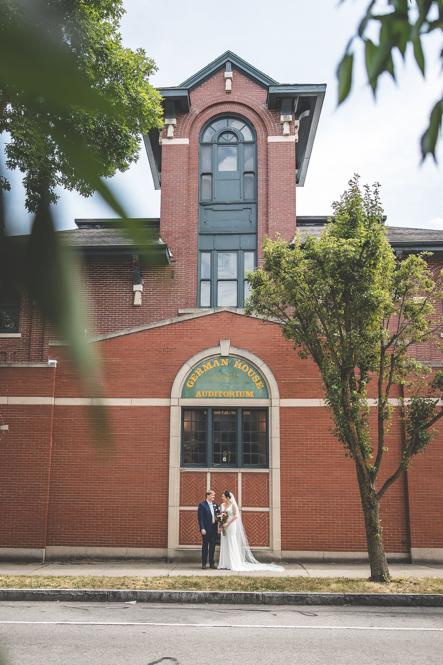 Elegant red brick building with arched windows serves as backdrop for wedding photos.